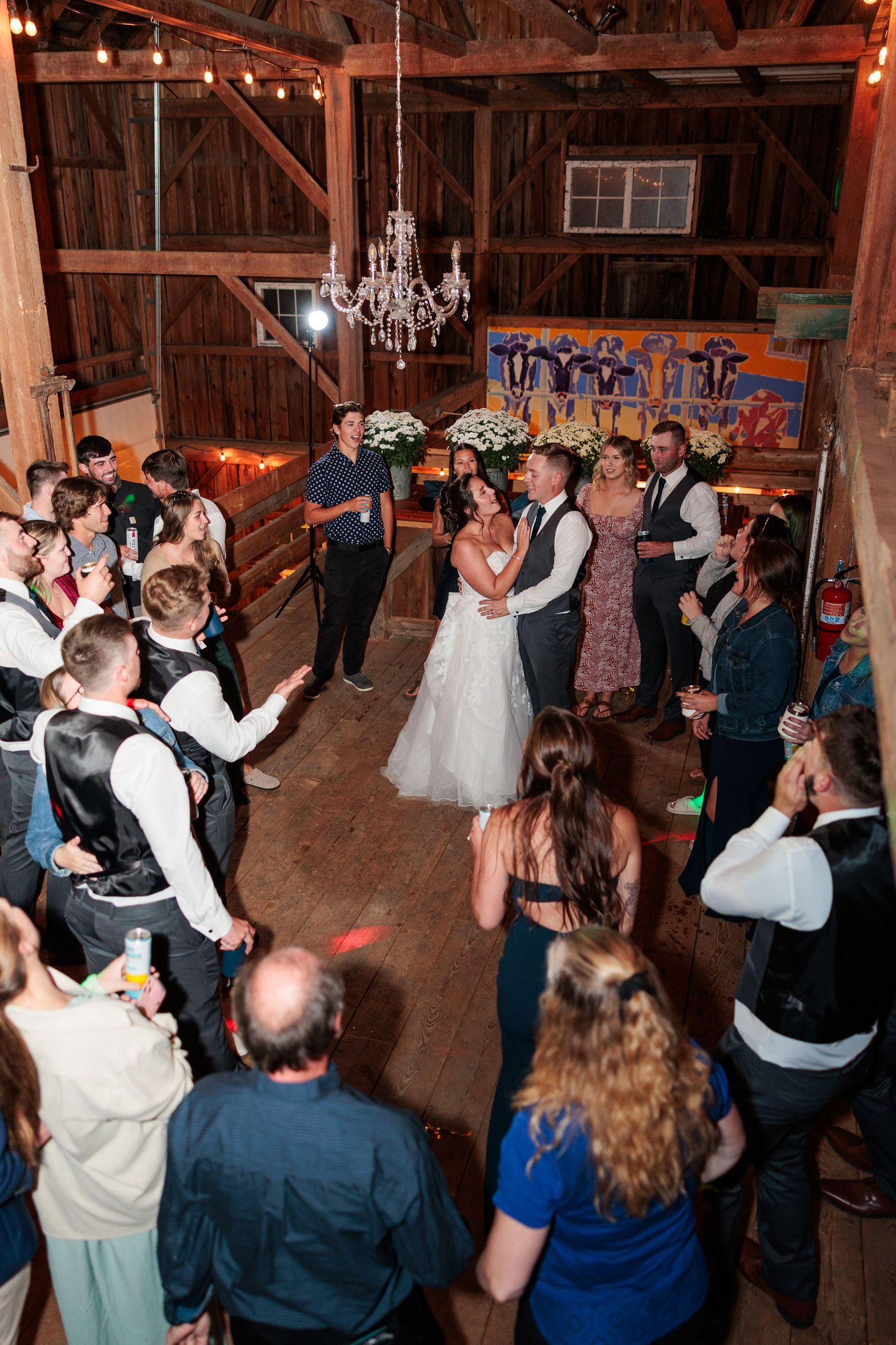Bride and groom share their first dance in a rustic barn as guests form a circle around them.