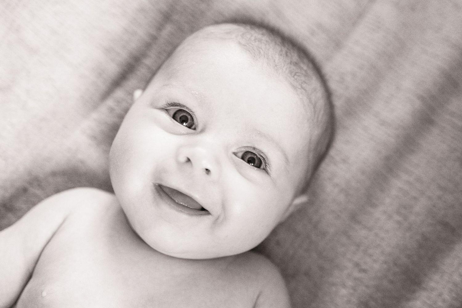 Black and white portrait of smiling baby with bright eyes looking directly at camera.