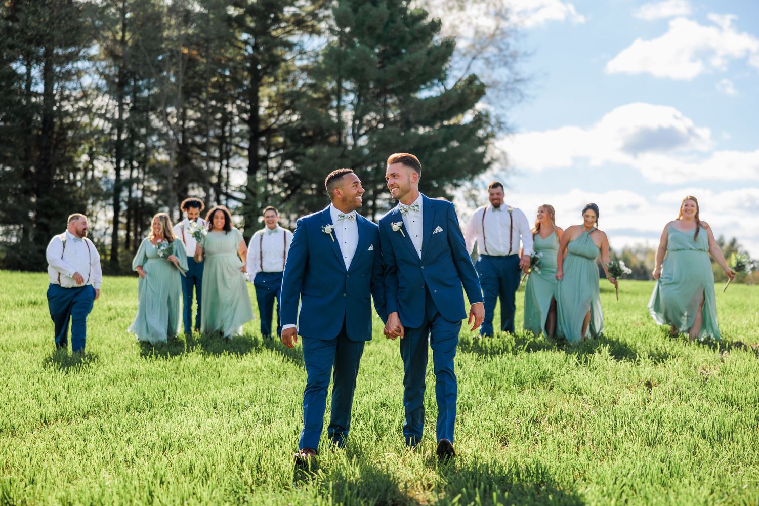 Wedding party members stand scattered across sunny lawn in coordinated mint green and navy blue attire.