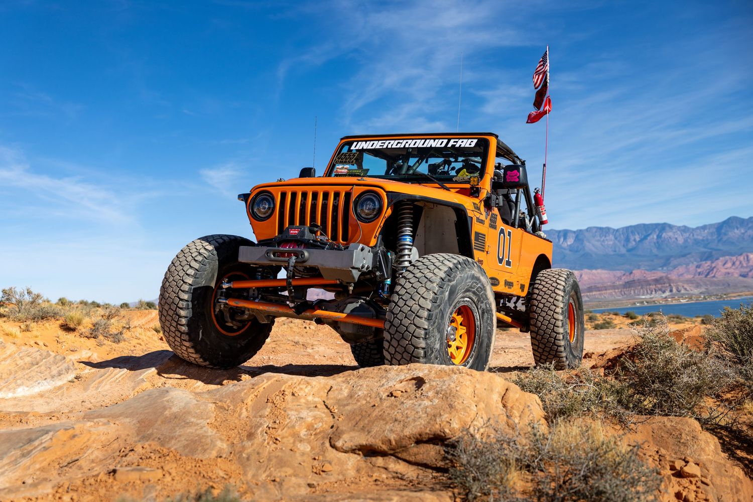 Orange Underground Pro lifted Jeep Wrangler rock crawling on desert terrain with Arizona flag.