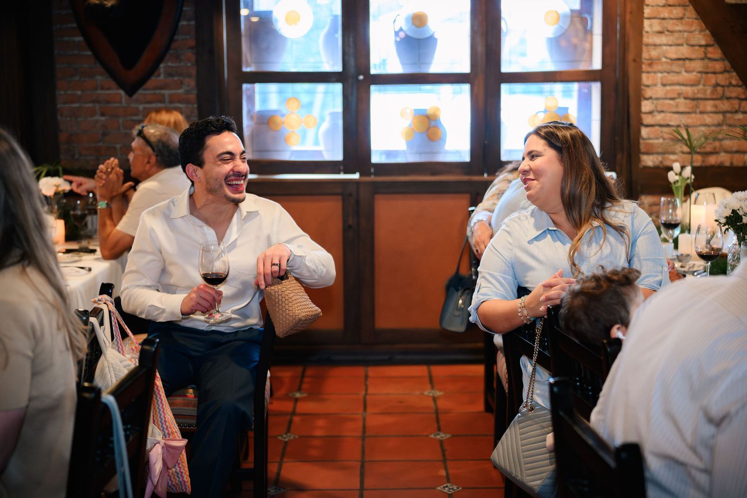 Guests mingling and laughing during a social event in a rustic restaurant setting with brick walls.
