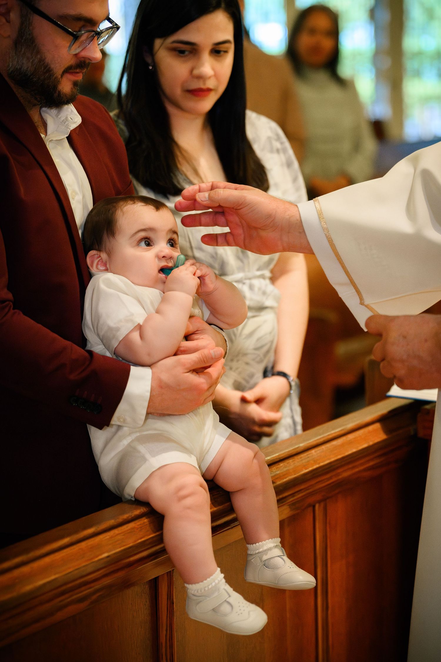 A baby in white clothing receives a baptismal blessing during a church ceremony.