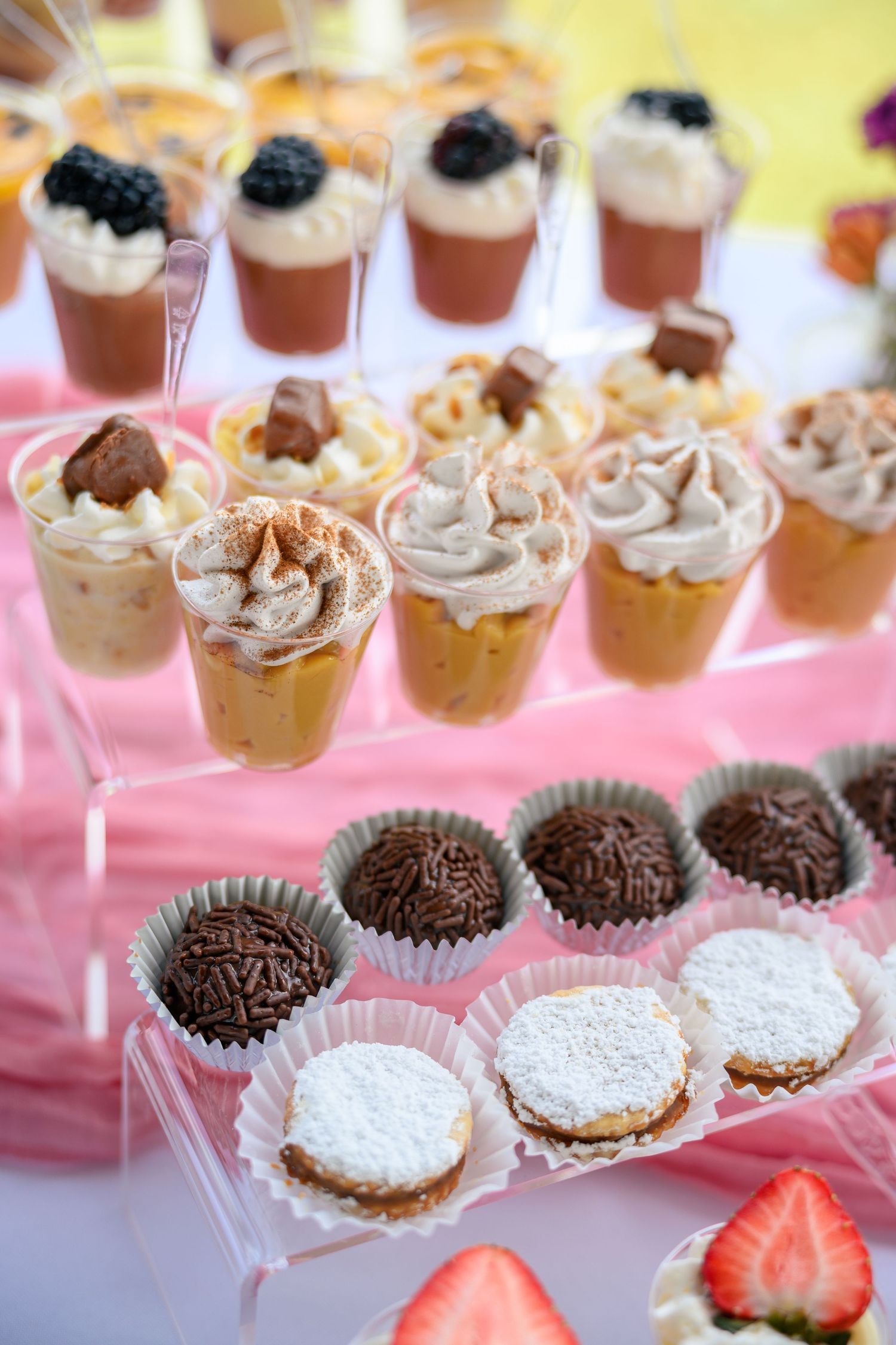 Elegant dessert display featuring chocolate truffles, whipped cream topped drinks, and fresh strawberries on a pink table.