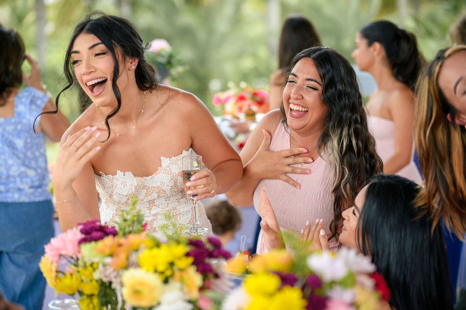 Wedding guests share joyful laughter at a colorful outdoor reception table decorated with yellow flowers.