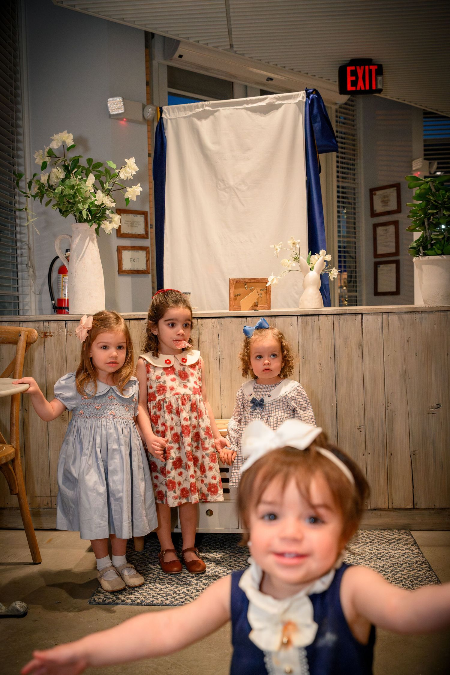 Young children stand together in a row wearing vintage-style clothing at what appears to be a church or community event.