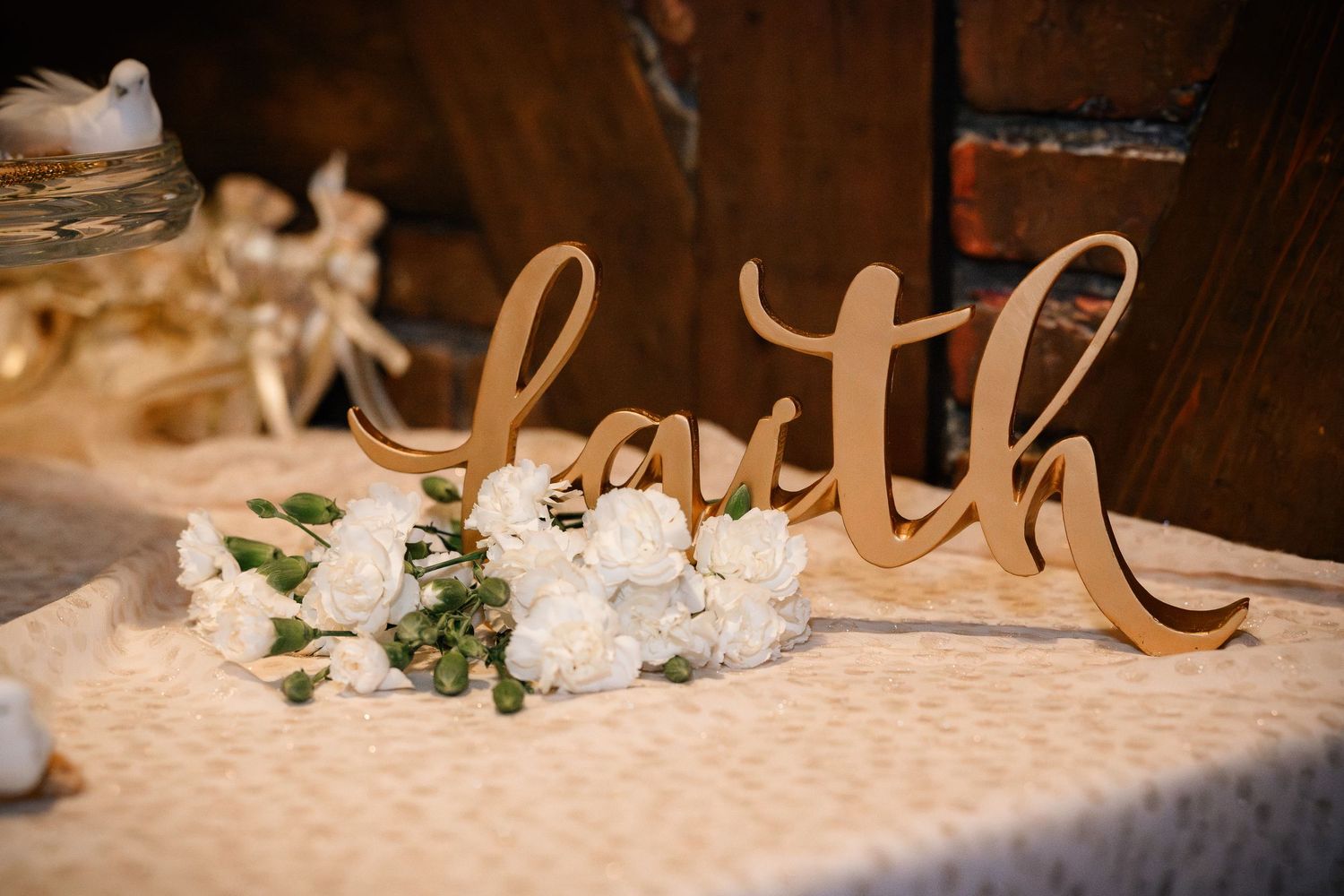 Elegant wedding reception table decor features gold script lettering and delicate white floral arrangements.