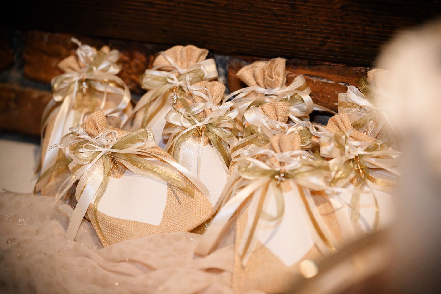 Row of cream-colored wedding favor boxes with gold ribbons arranged on wooden surface.