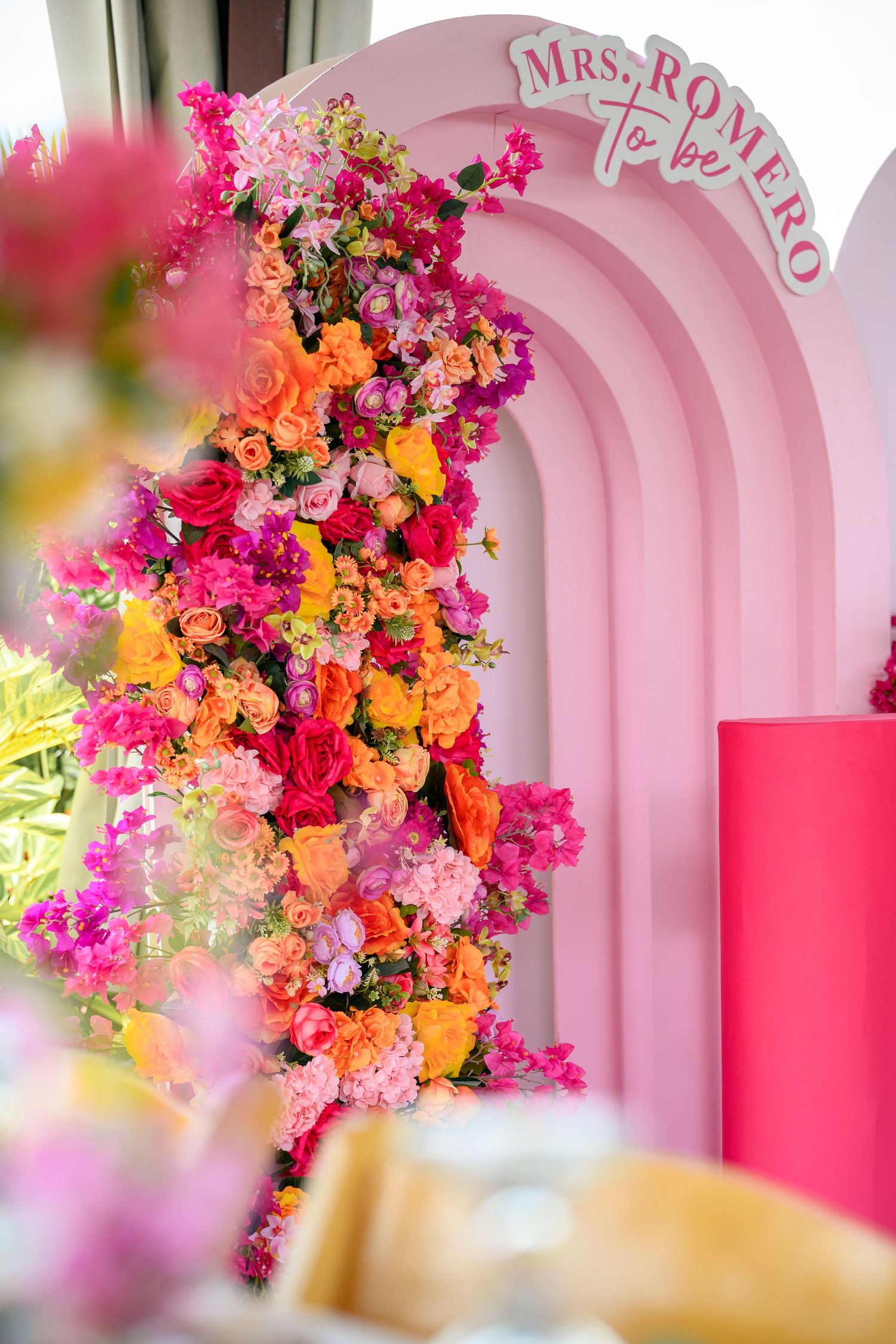 Vibrant pink and orange floral arrangement cascades down a pink arched backdrop with 'Mrs Romeo' text signage.