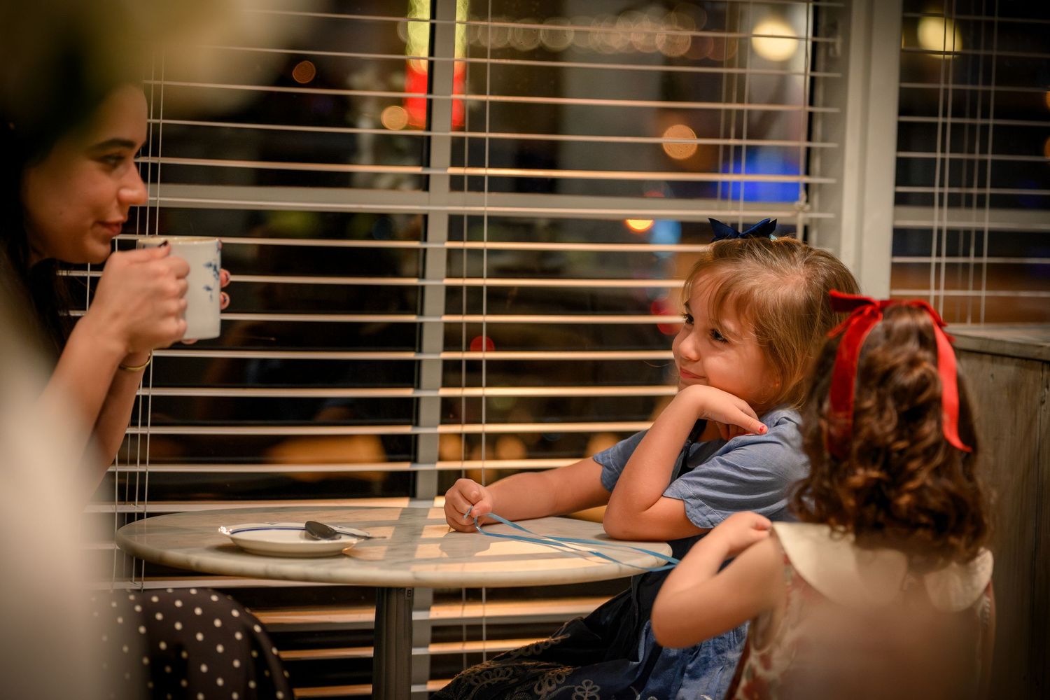 Group of people enjoying drinks and conversation at a cozy indoor gathering with window blinds in the background.