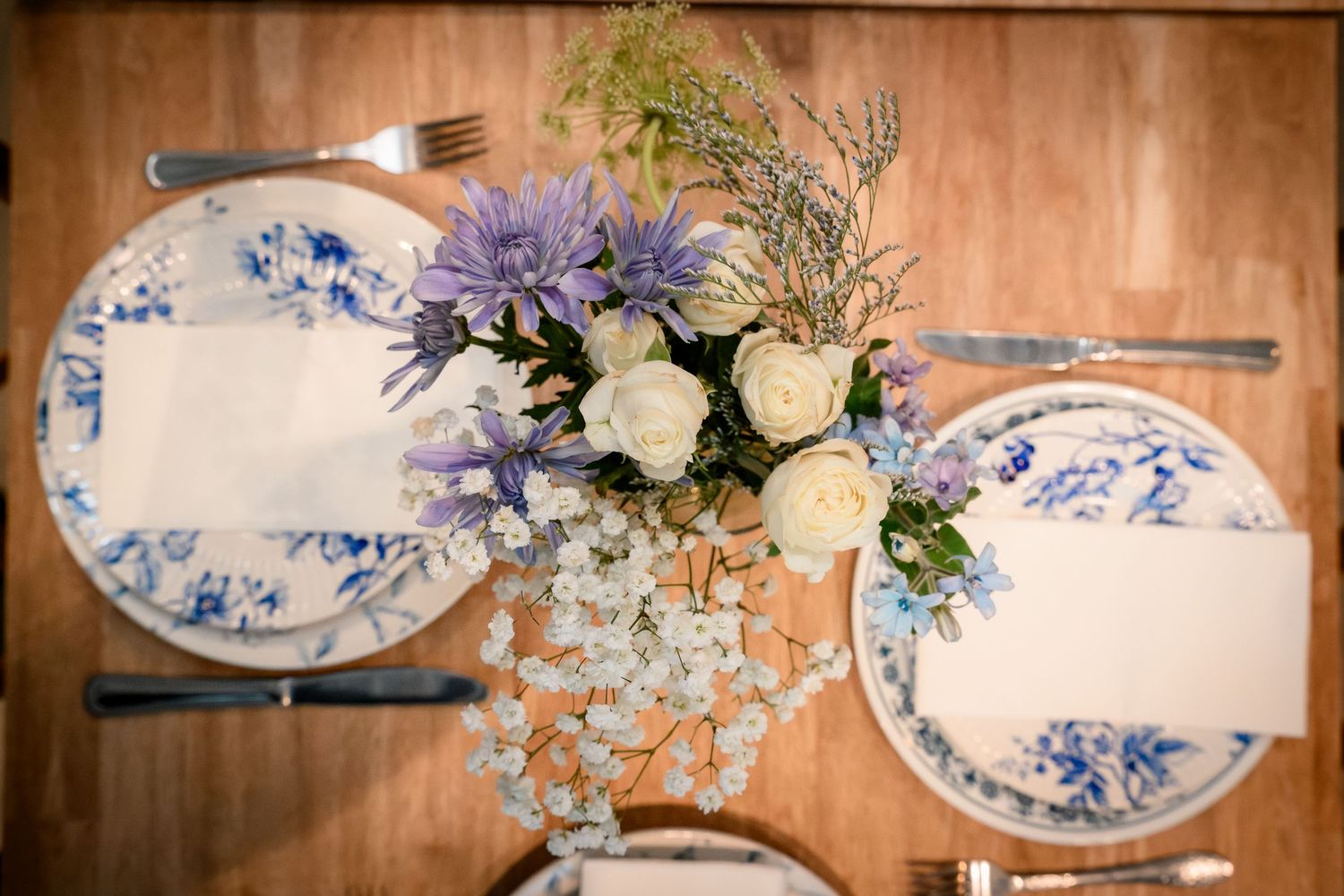 Elegant table setting with blue and white floral plates, purple and white flower centerpiece arrangement.