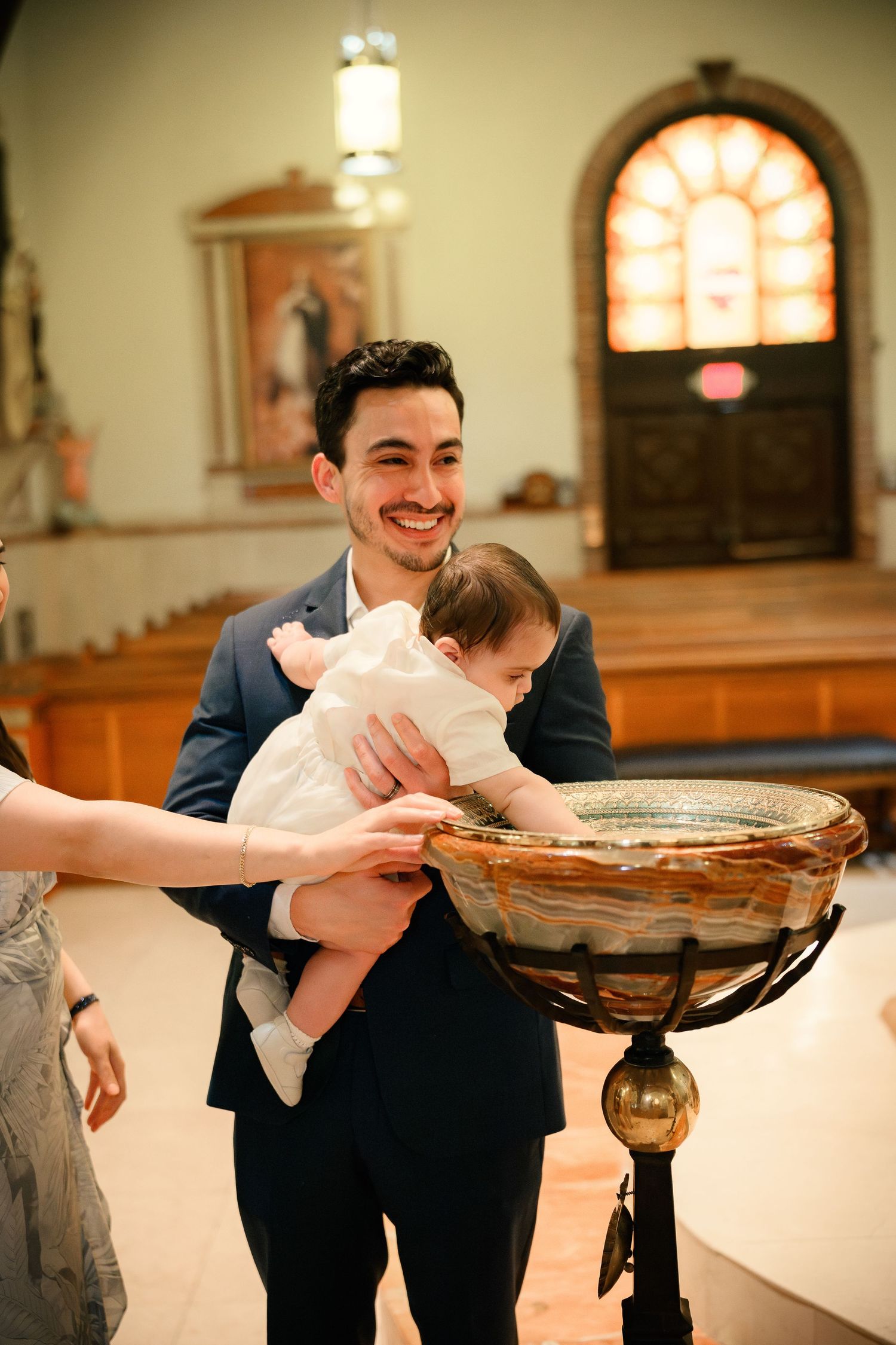 A person in a navy suit bends down to smell a large pie on a decorative metal stand in a church setting.