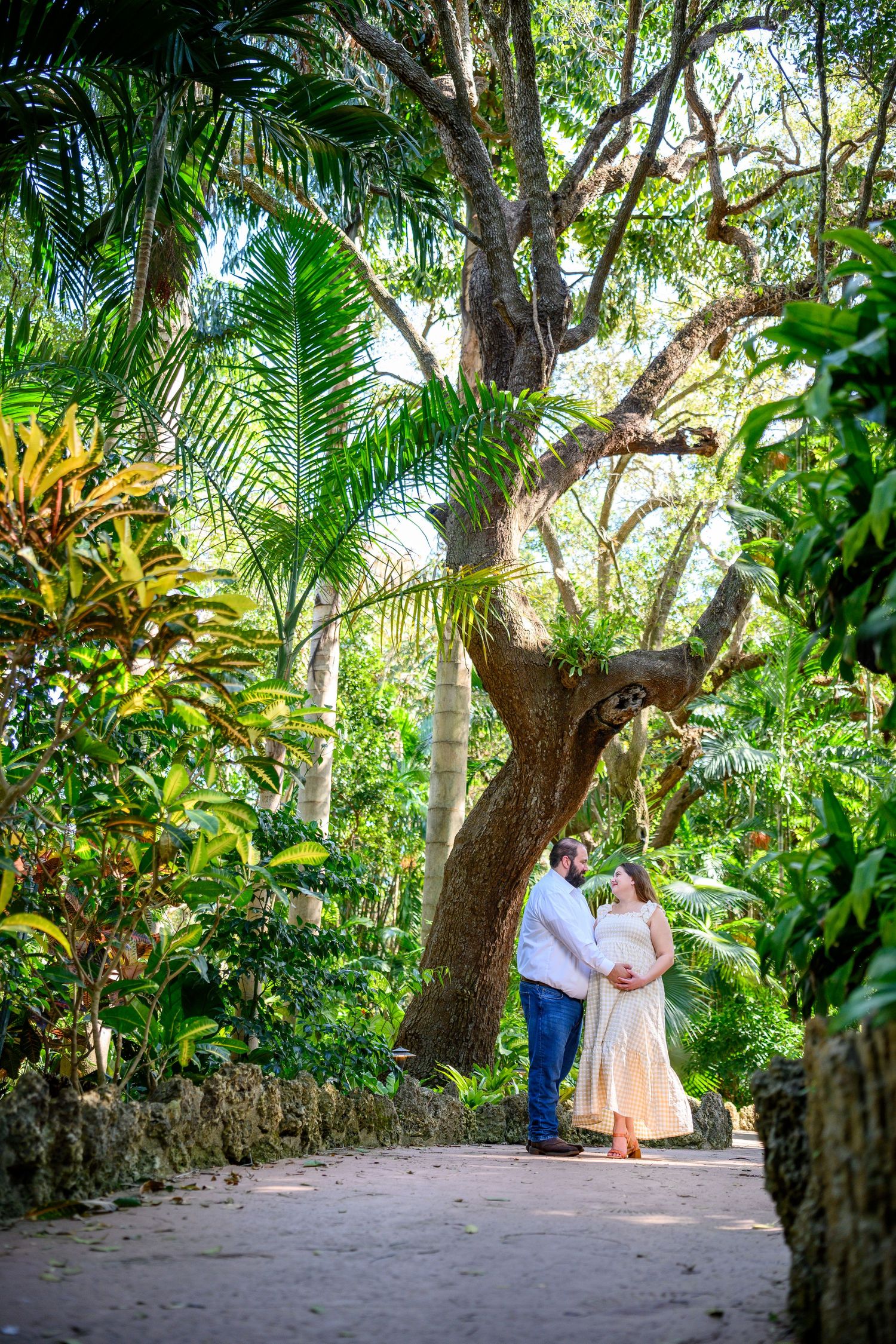 Romantic couple embraces on a lush tropical garden path surrounded by palm trees and greenery.
