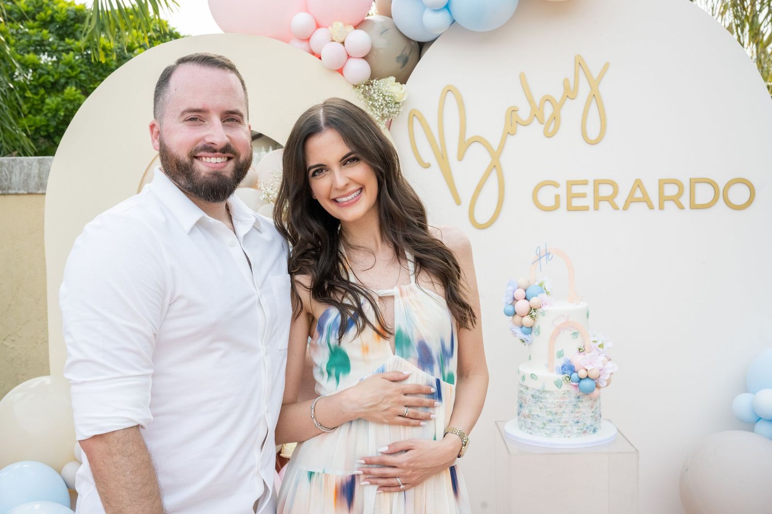 Couple poses at Baby Gerardo gender reveal party with balloons and decorated cake.