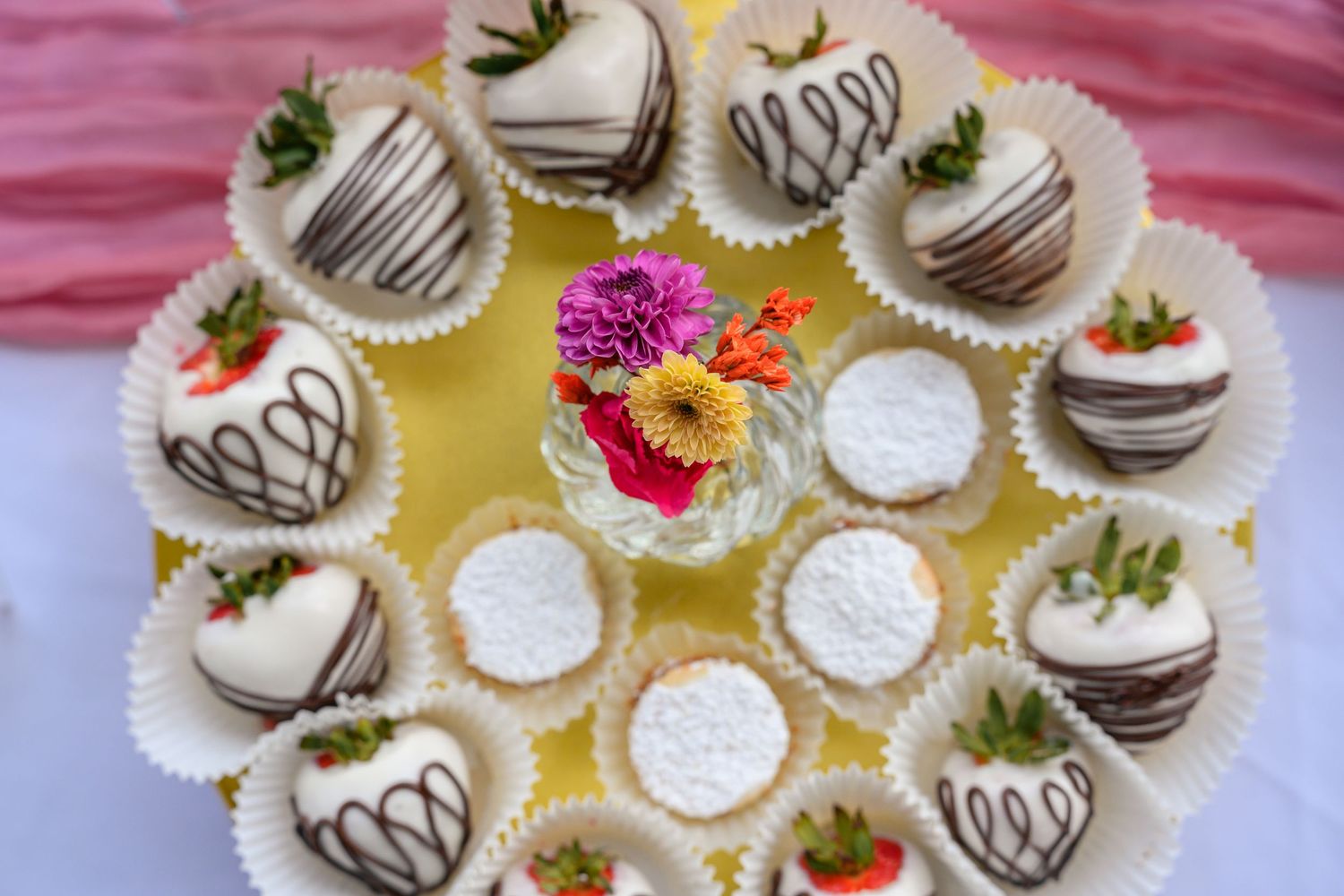 White chocolate covered strawberries arranged on a serving platter with pink and yellow flowers as decorative garnish.