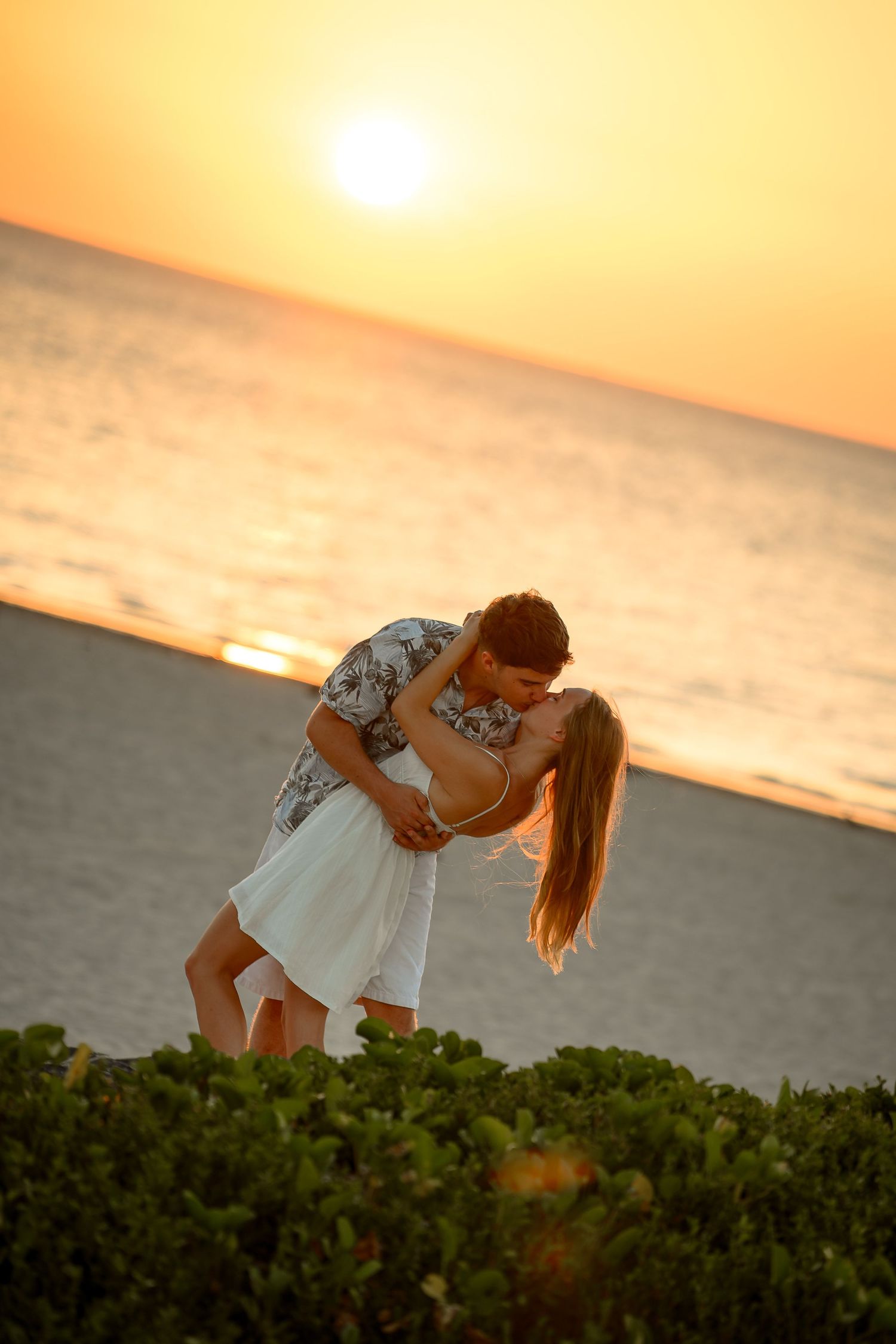 Couple sharing a romantic kiss on a beach at golden sunset with ocean waves in the background.