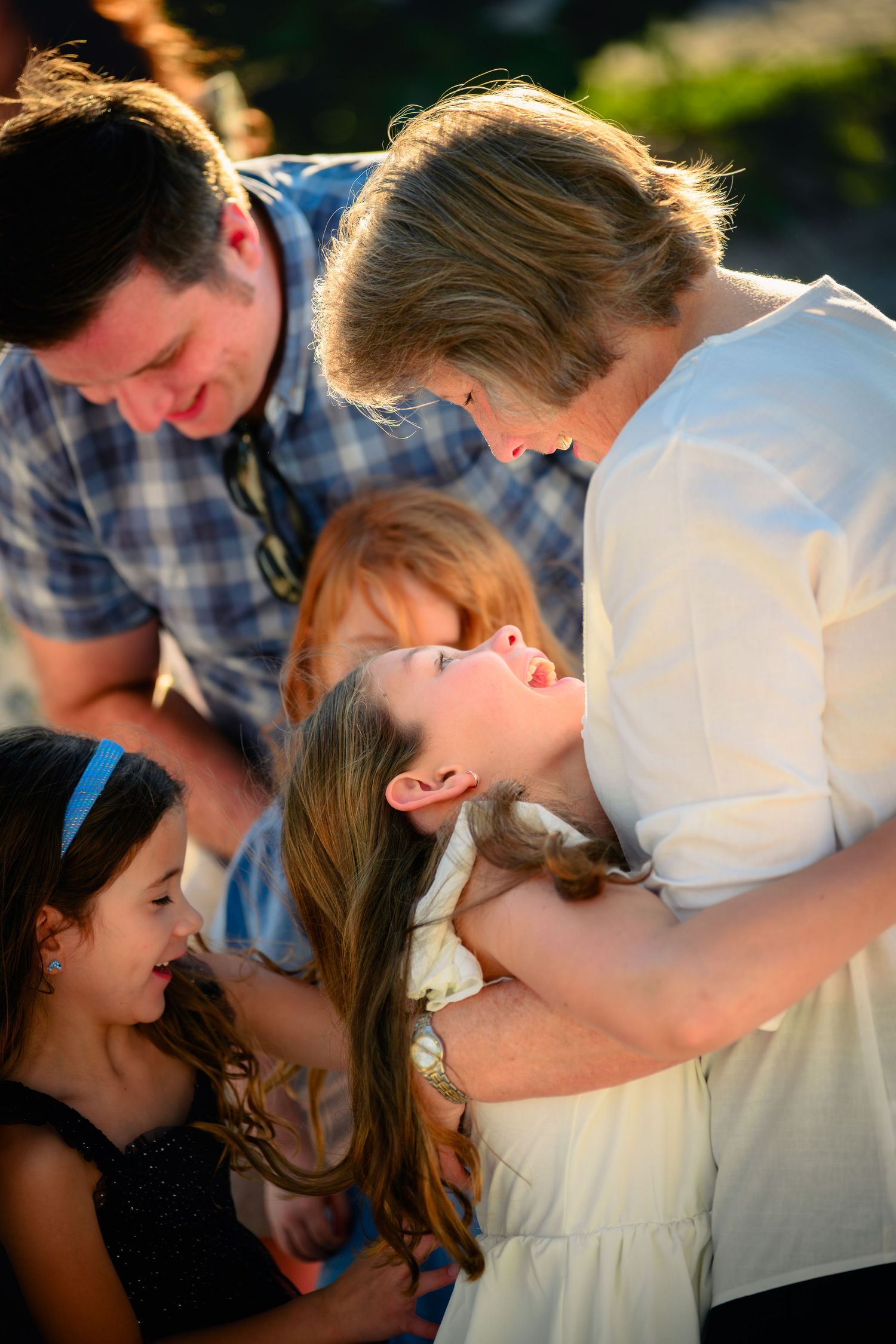 A warm family moment with parents and children sharing joy and laughter outdoors in golden sunlight.