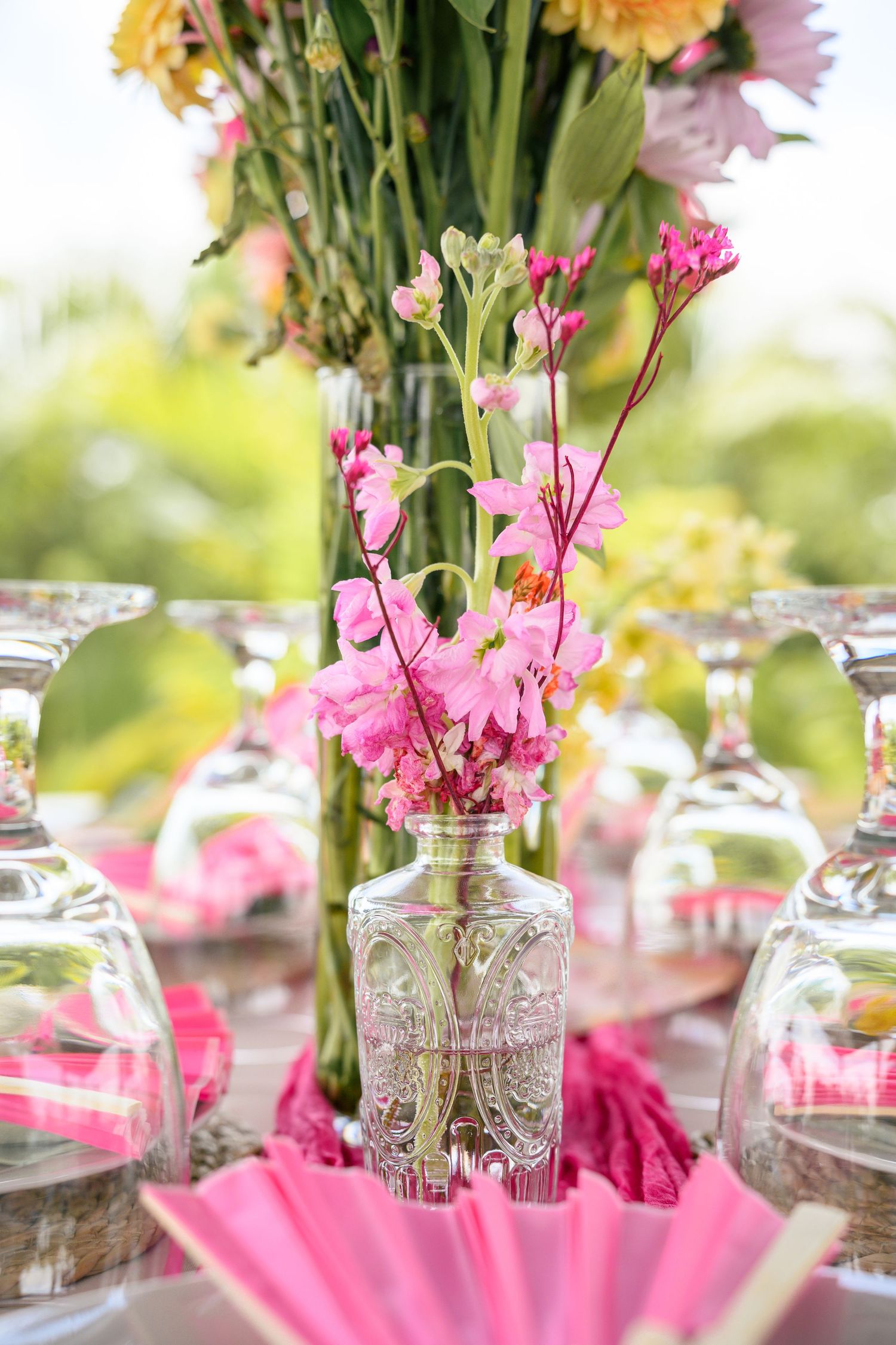 Pink flowers in crystal vases create an elegant table centerpiece display with soft bokeh background.