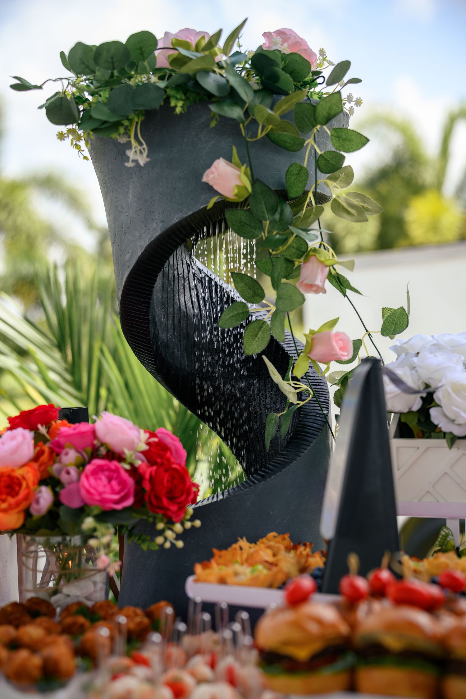 A catering display features decorated black chalkboard signs with floral arrangements and assorted appetizers on a table.