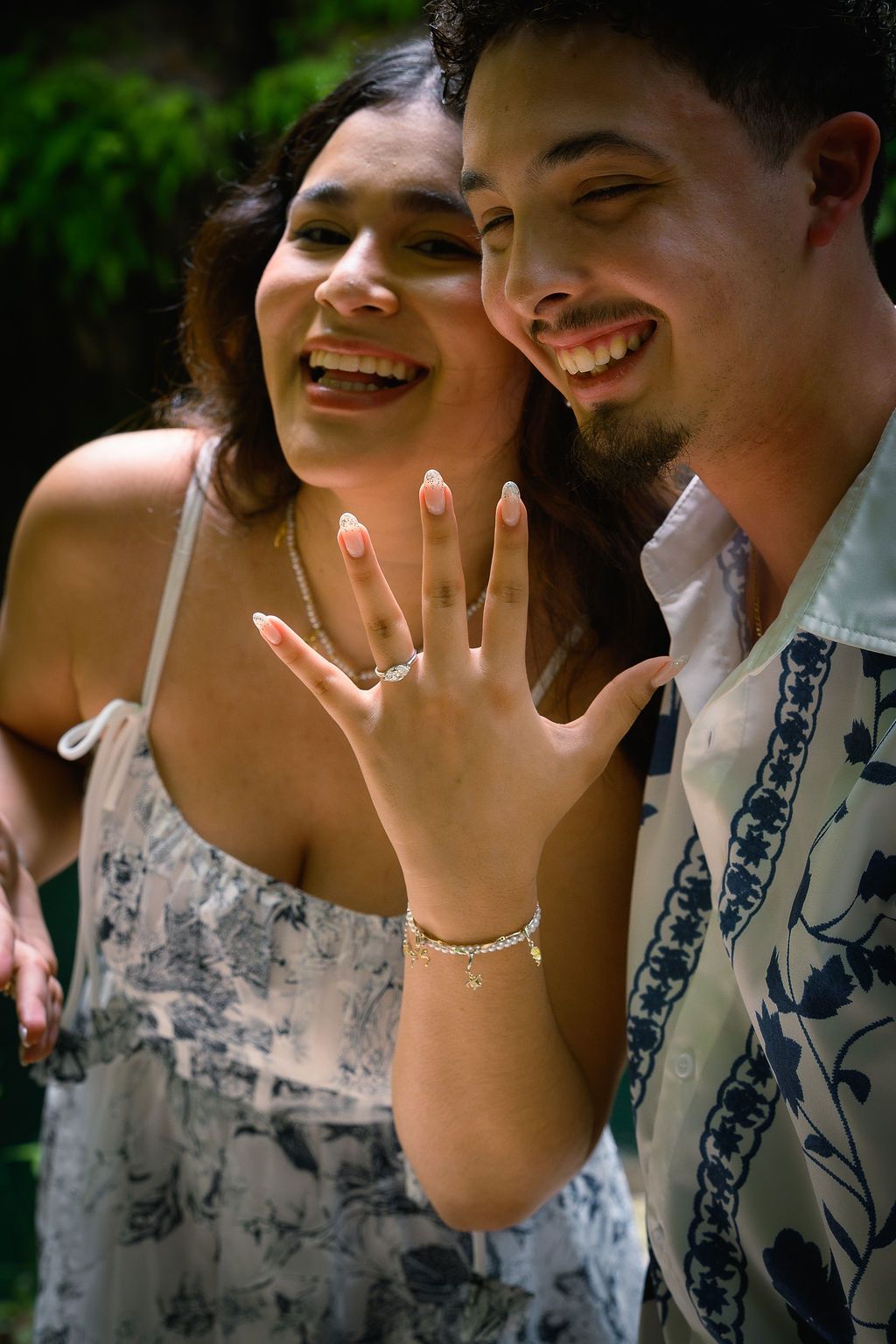 Happy couple smiling and showing off an engagement ring outdoors, celebrating their recent proposal.