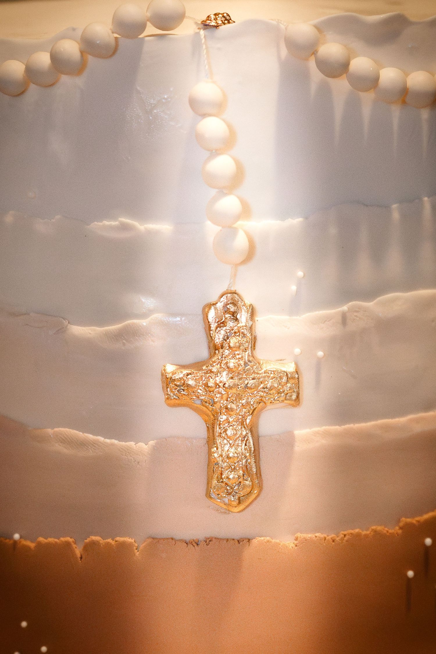 Ornate golden cross pendant hanging against a dramatic sunset sky with glowing white string lights in soft focus.