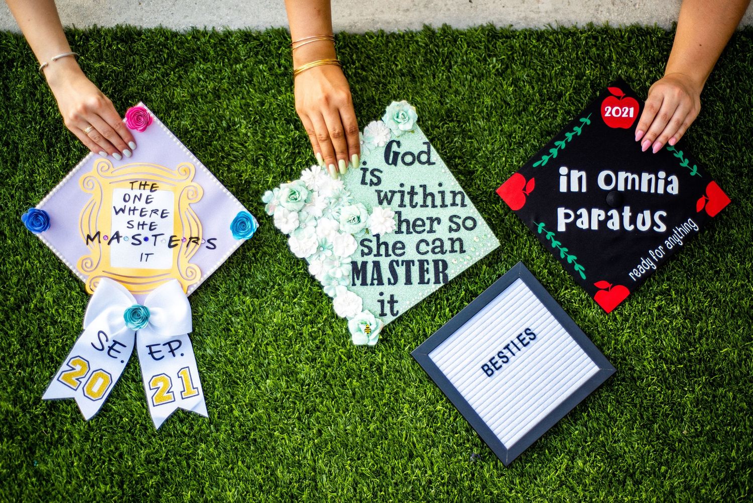 Three decorated graduation caps displayed on green grass with inspirational quotes and colorful designs.
