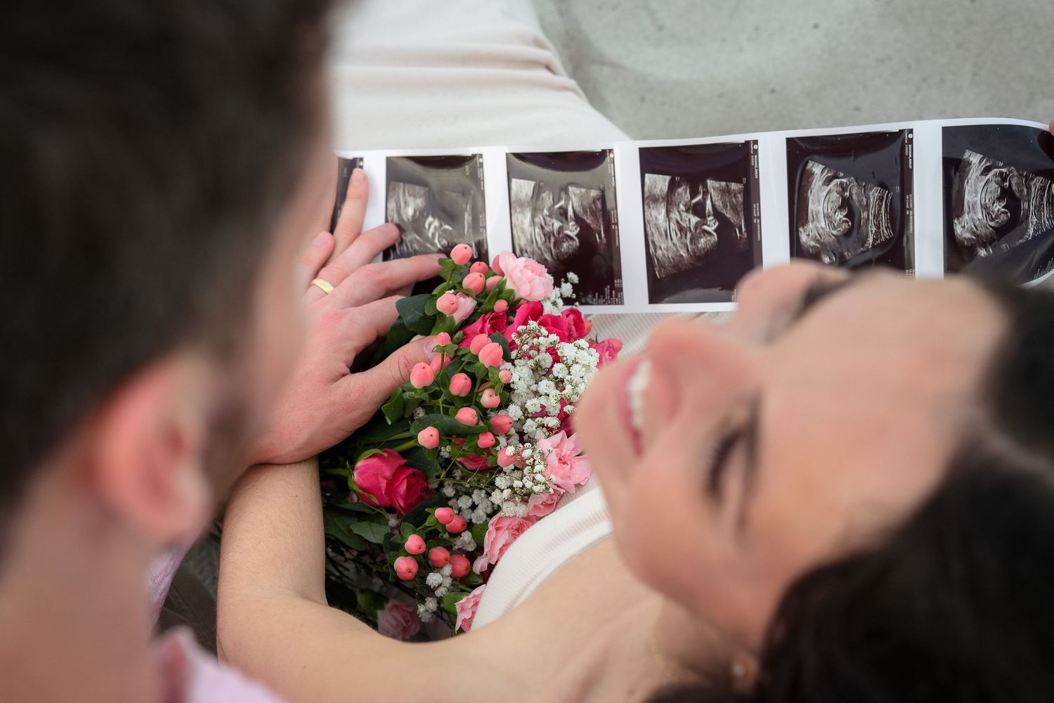 Couple sharing a tender moment with ultrasound photos and pink roses, celebrating pregnancy announcement.