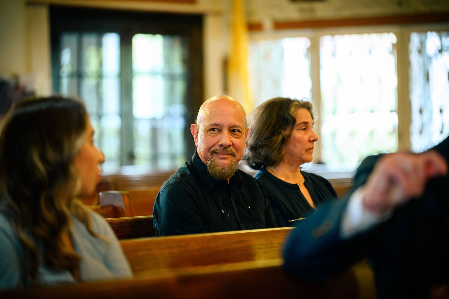People seated in wooden church pews during a service or gathering in a traditional sanctuary.