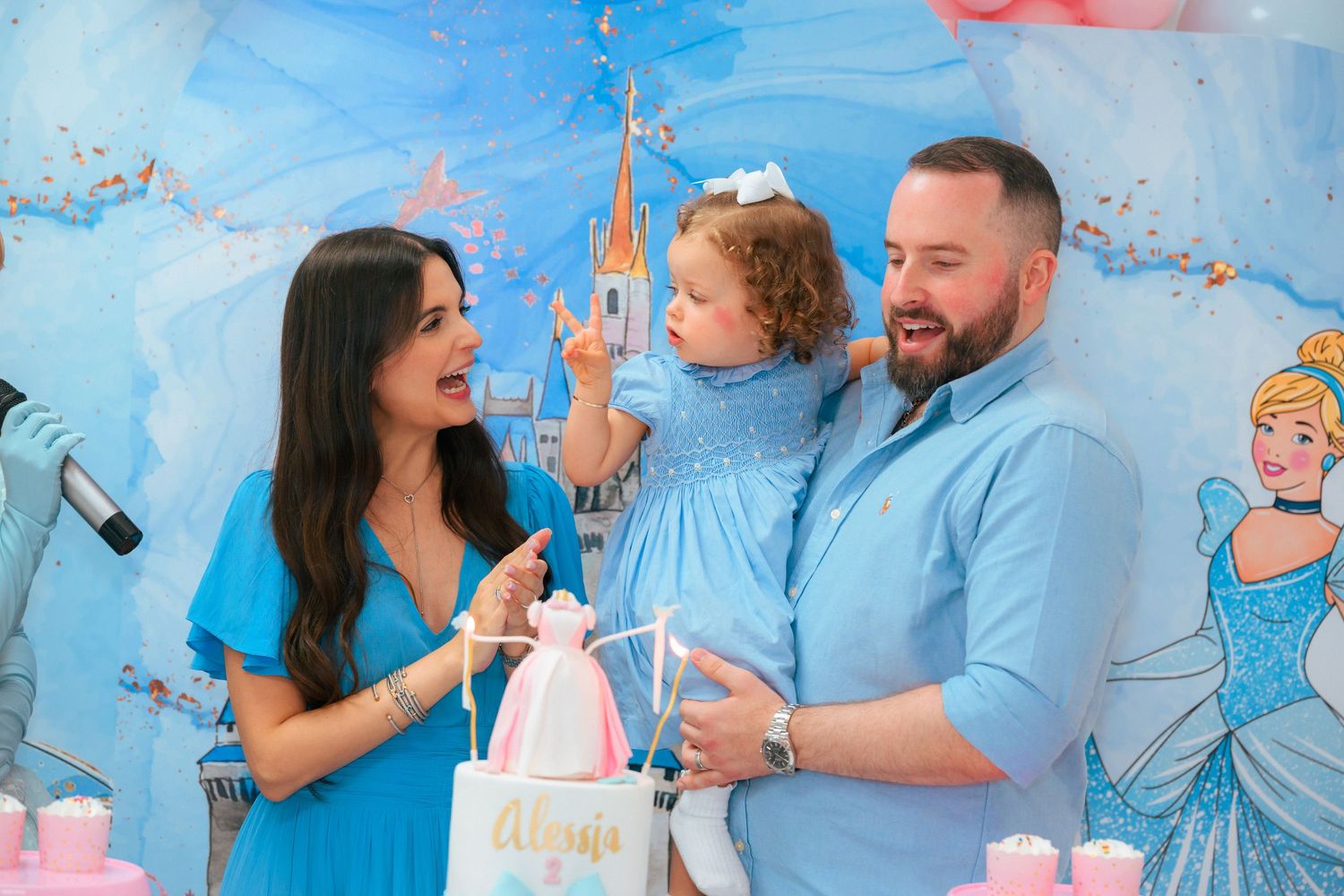 A family celebrates at a birthday party with a Cinderella-themed backdrop and decorations.