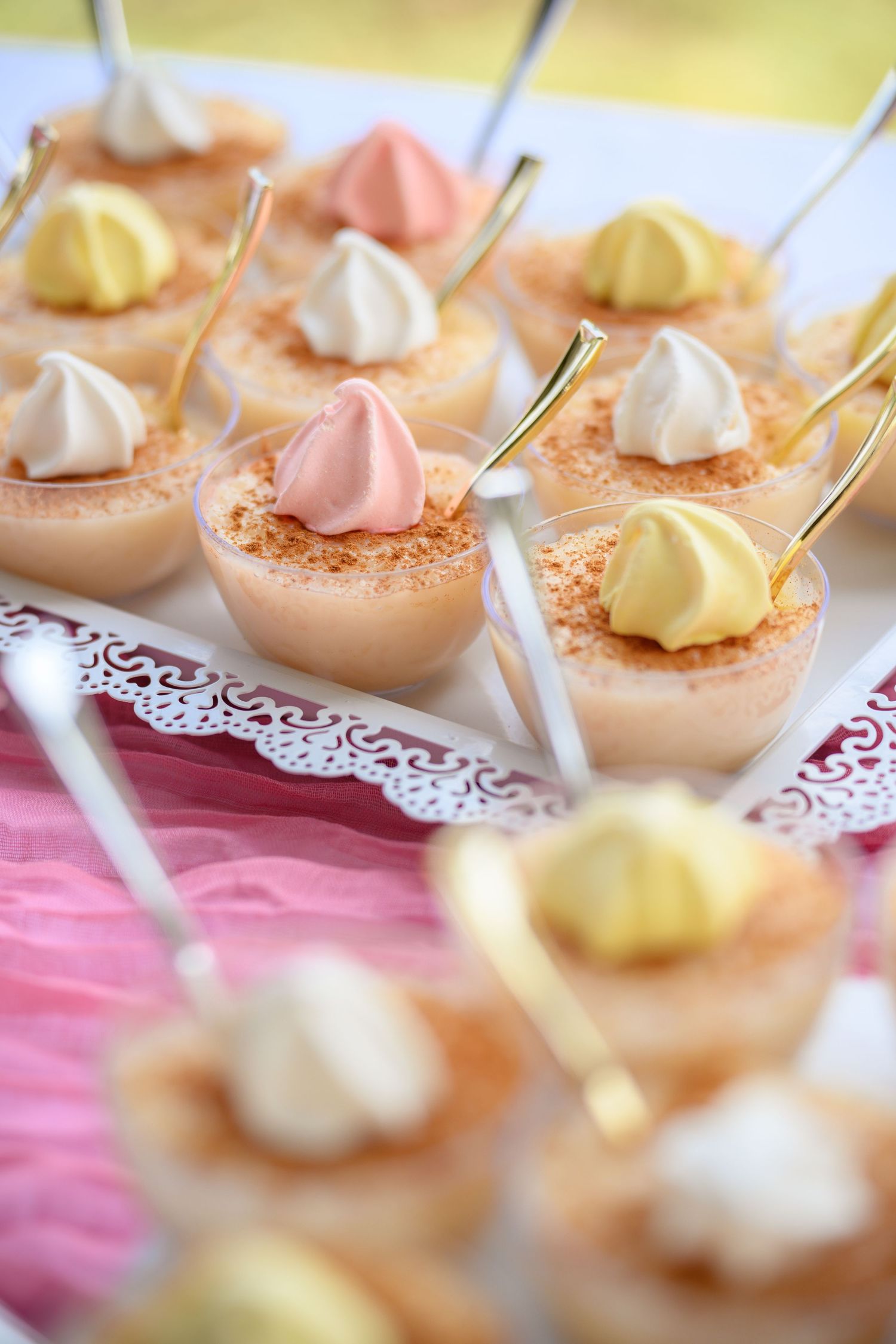 Small pastel-colored dessert bites topped with whipped cream dollops on delicate white doilies.