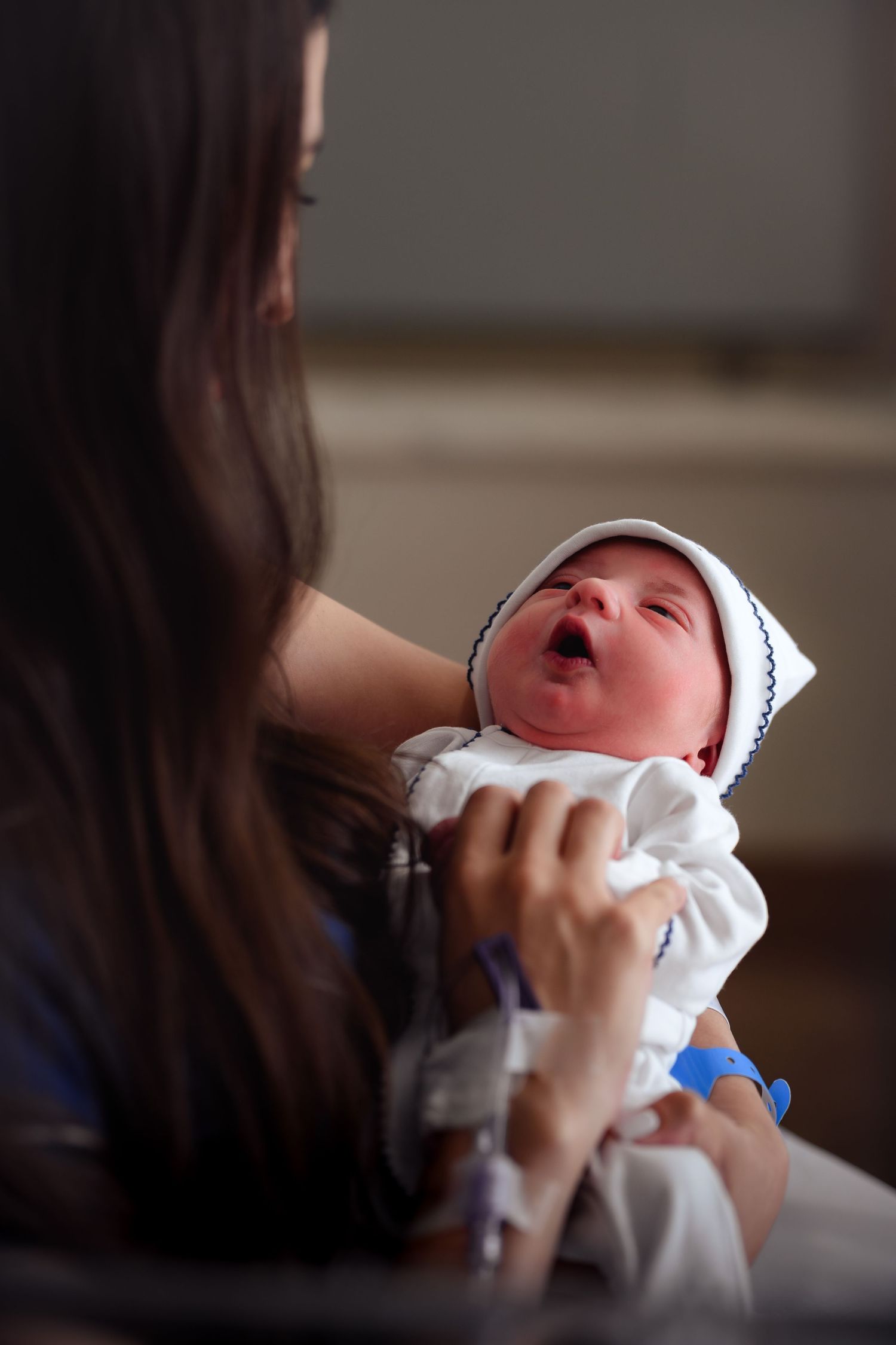 A crying newborn baby wrapped in white cloth being held and comforted.