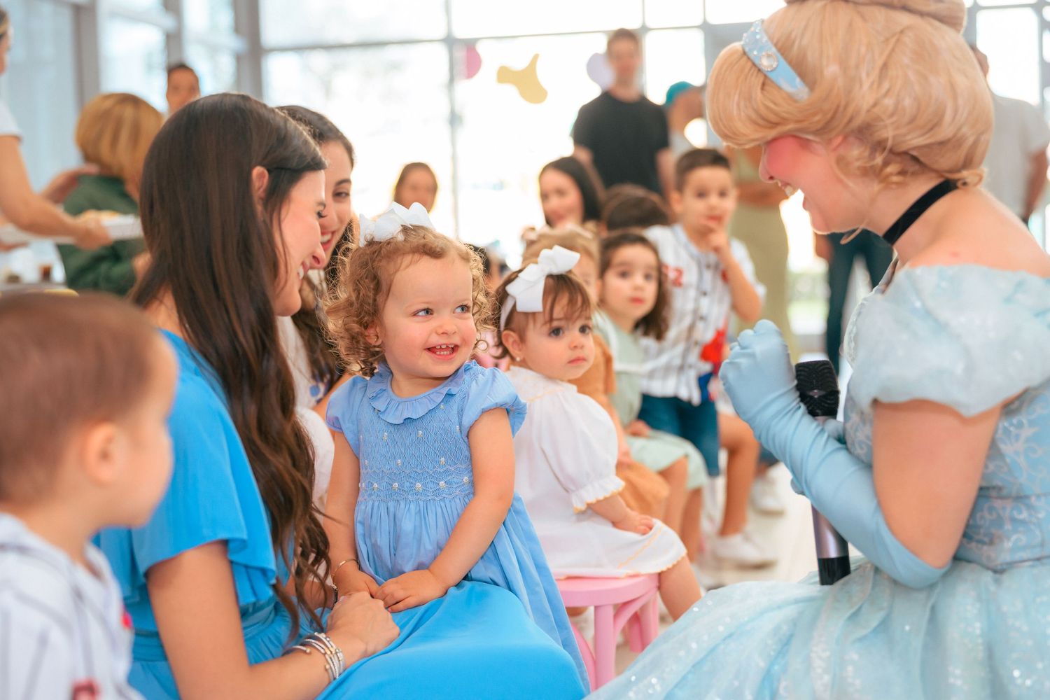 A little girl in a blue dress smiles delightedly while meeting a Cinderella princess character.