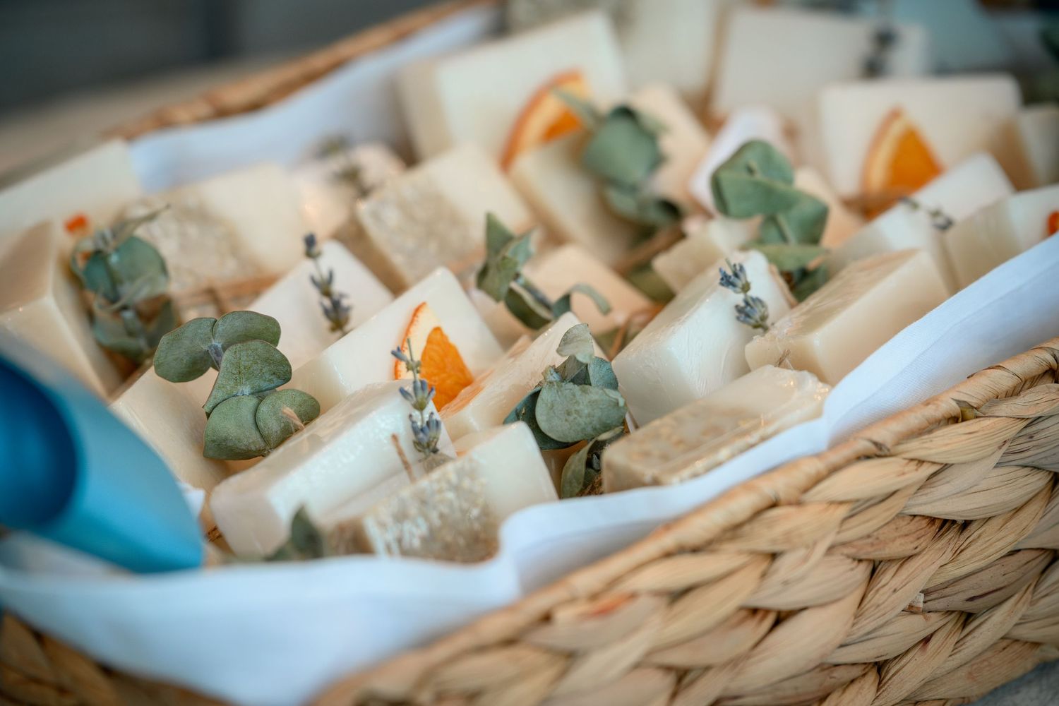 Artisan soaps with eucalyptus and botanical accents arranged in a wicker basket lined with white tissue paper.