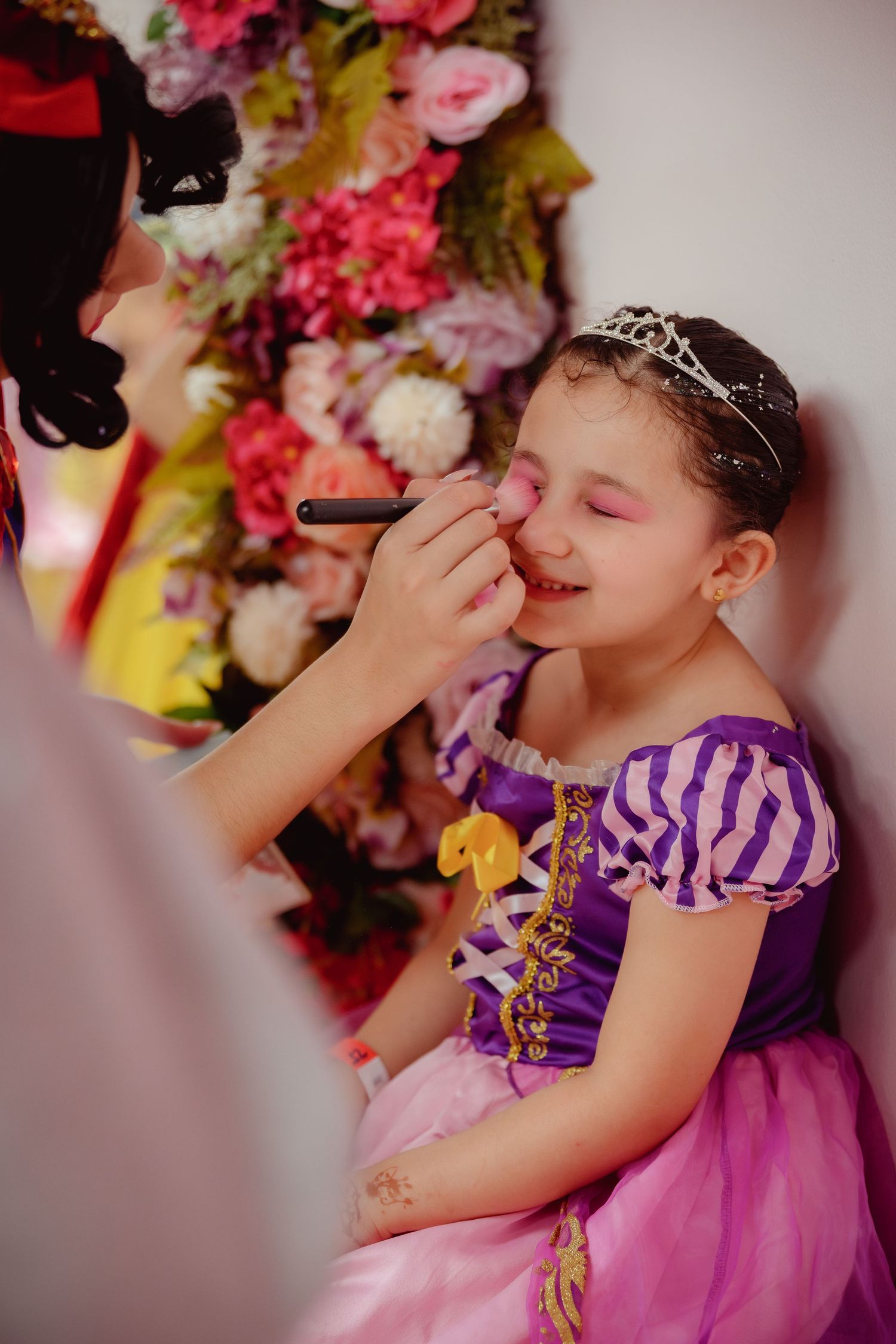Young girl in purple princess dress getting face paint applied at a birthday party celebration.