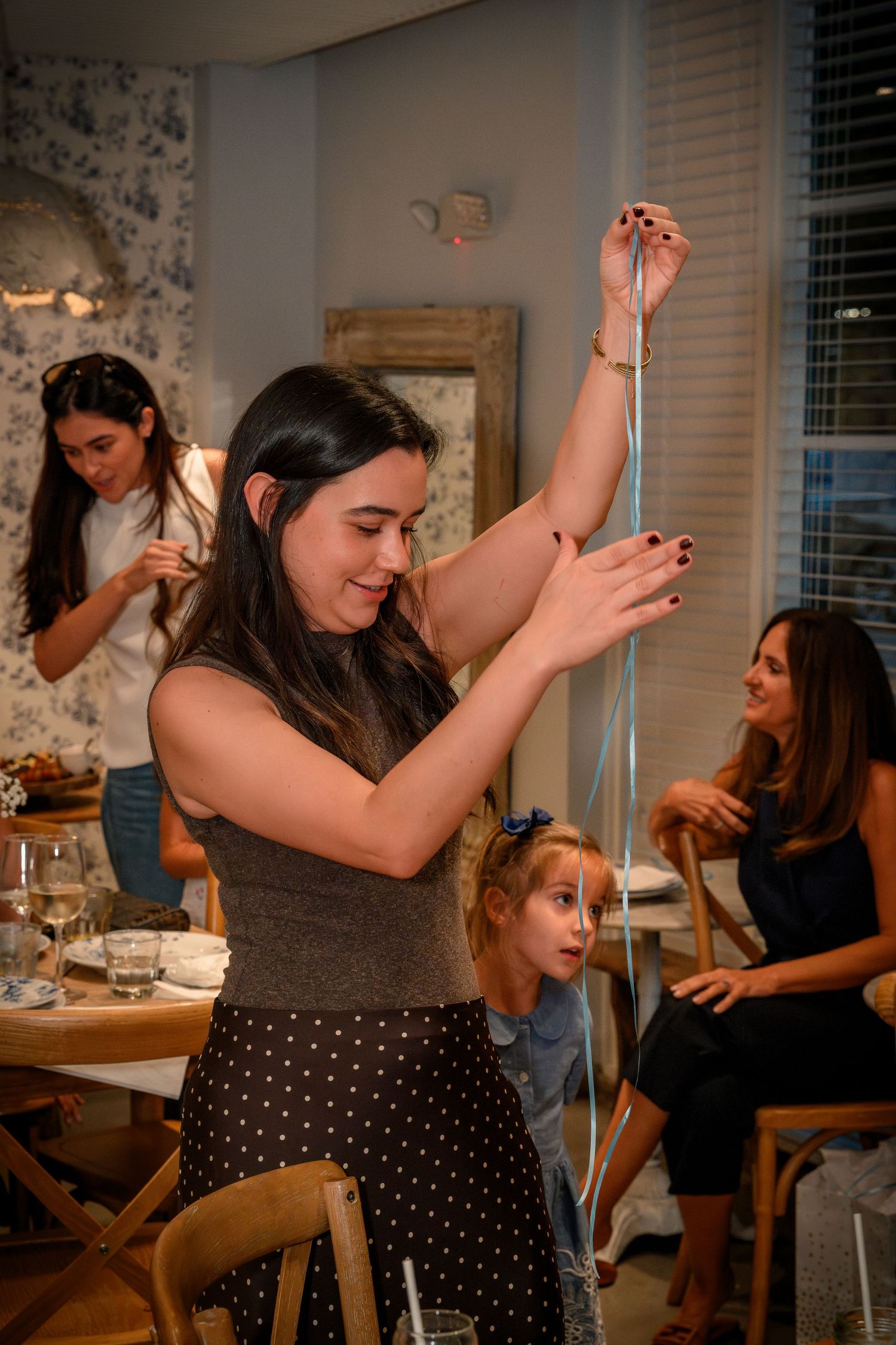 People gathered around a dining table enjoying a lively celebration with raised arms and animated expressions.