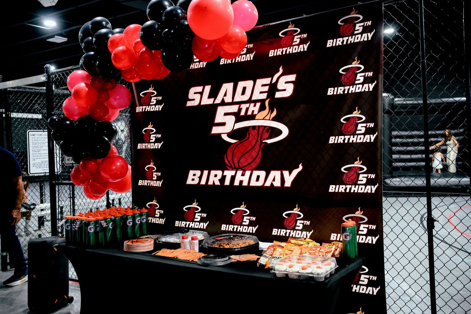 Miami Heat themed 5th birthday party backdrop with red and black balloons, food table, and personalized Slade's birthday banner.