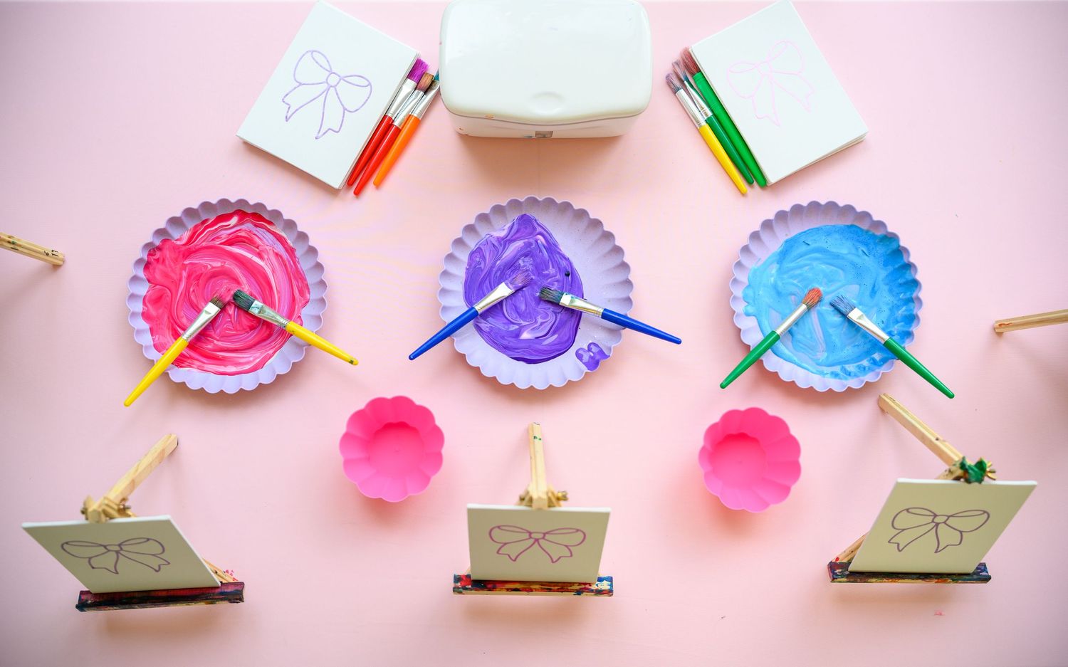 Colorful paper plates transformed into creative craft projects with popsicle sticks and paint on a pink background.