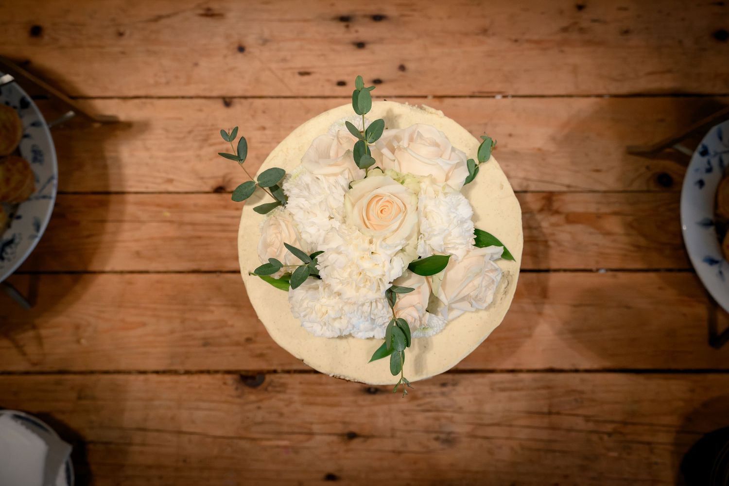 White roses and greenery arranged on rustic wooden boards create an elegant table setting.