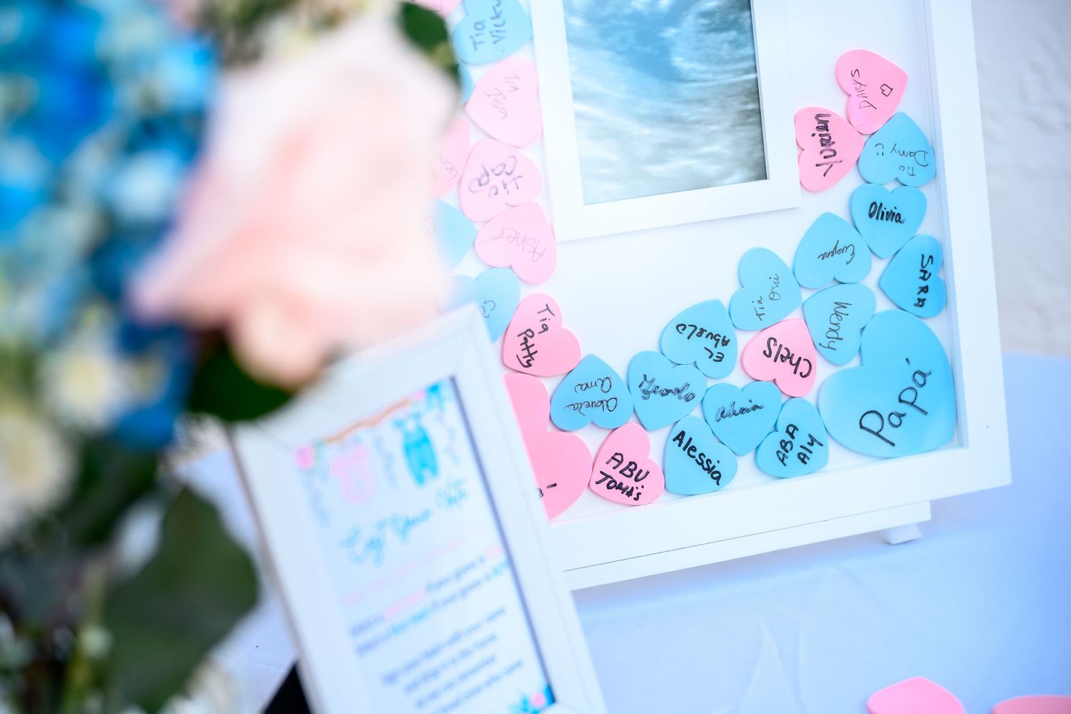 Gender reveal party guest book with pink and blue heart notes on white frame display.