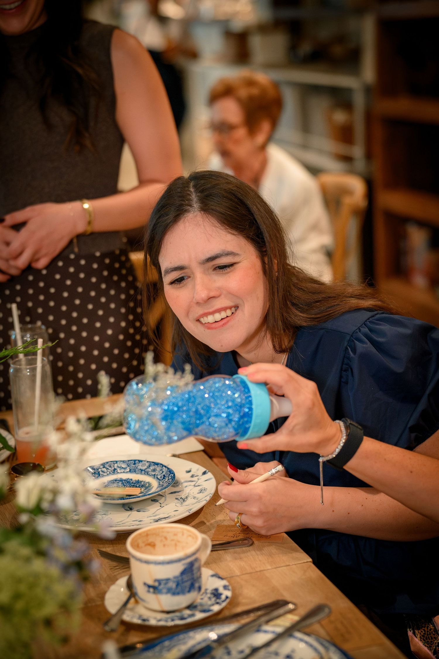Young woman smiling while opening a blue glittery gift at a festive bridal shower celebration.