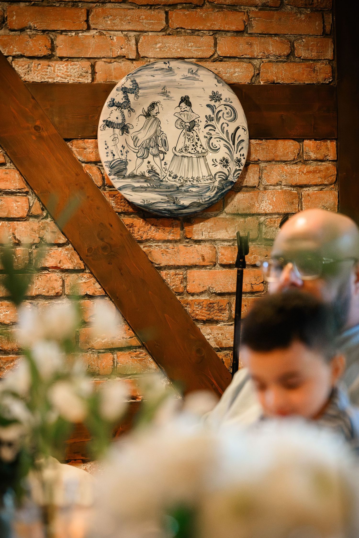 Decorative vintage plate with pastoral scene mounted on exposed brick wall above dining area.