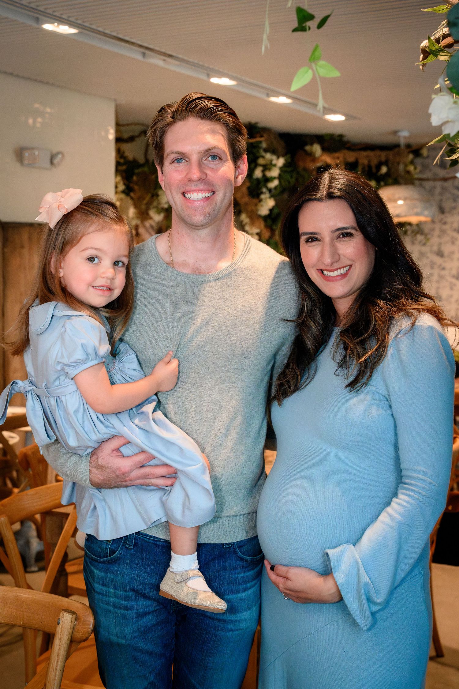 A family in coordinating light blue outfits poses together in an indoor setting.