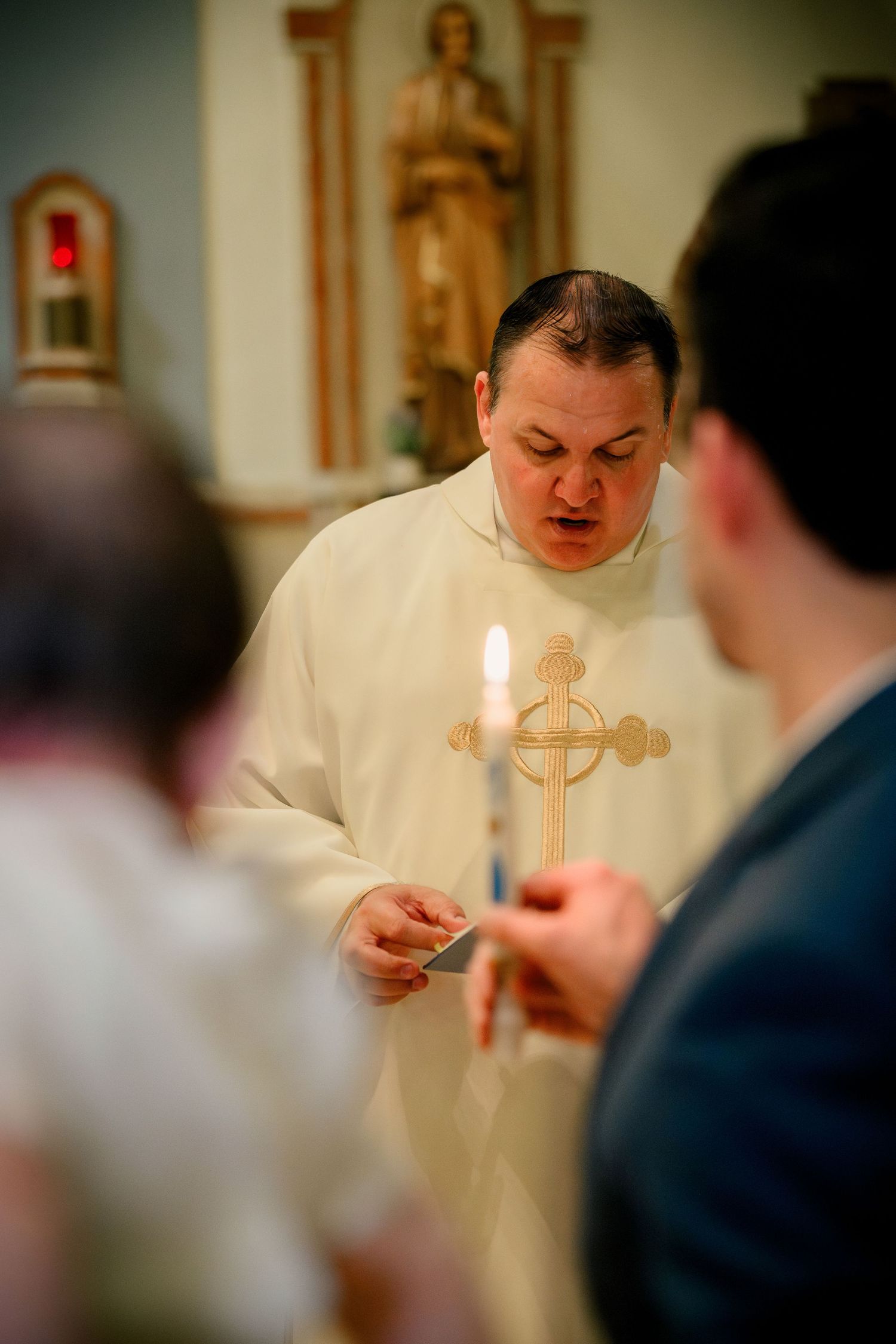 A priest in white vestments lights candles during a religious ceremony.
