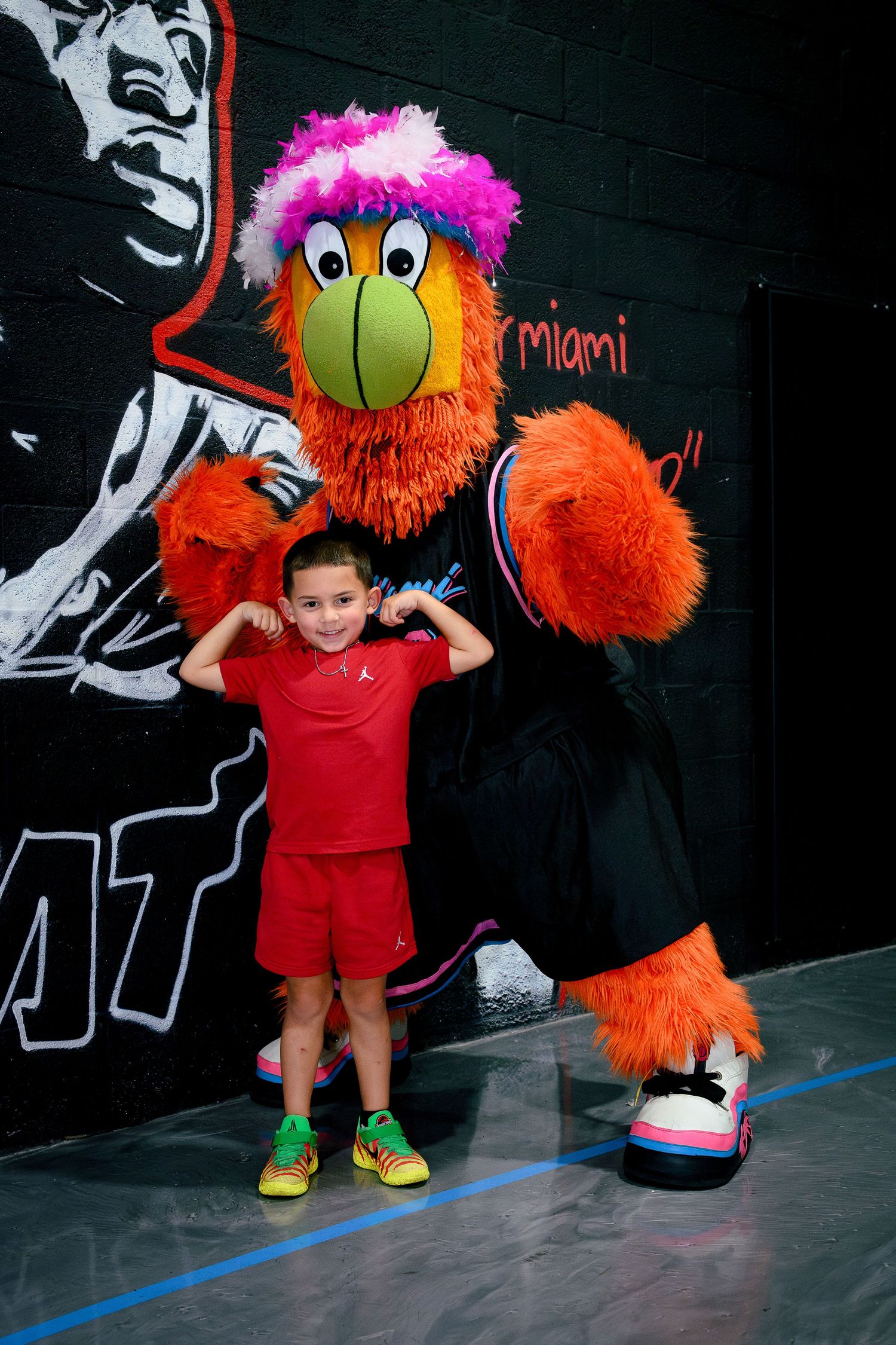 Young boy flexing with Miami Heat mascot Burnie at a Miami Heat basketball event.