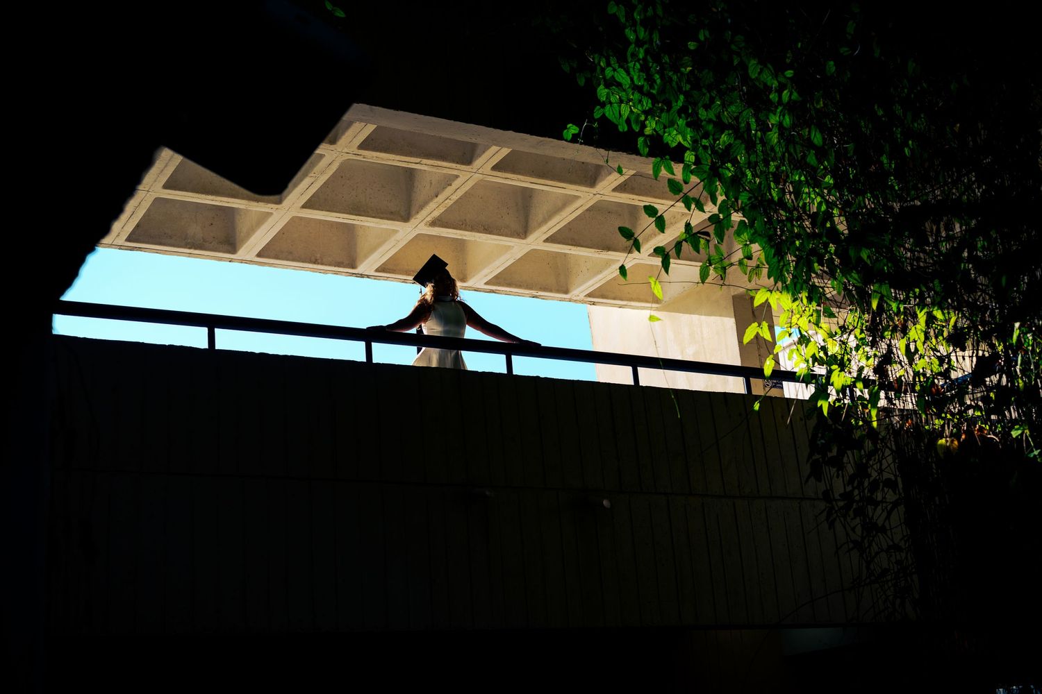 Silhouette of a person standing on a balcony at night under illuminated skylight.