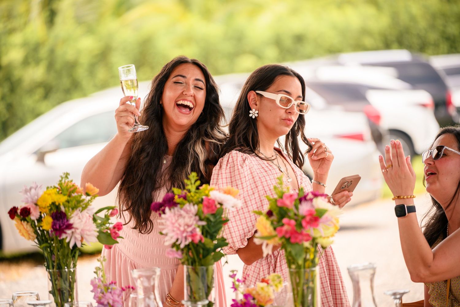 A group of friends celebrate at an outdoor party with champagne glasses and colorful flower arrangements on the table.