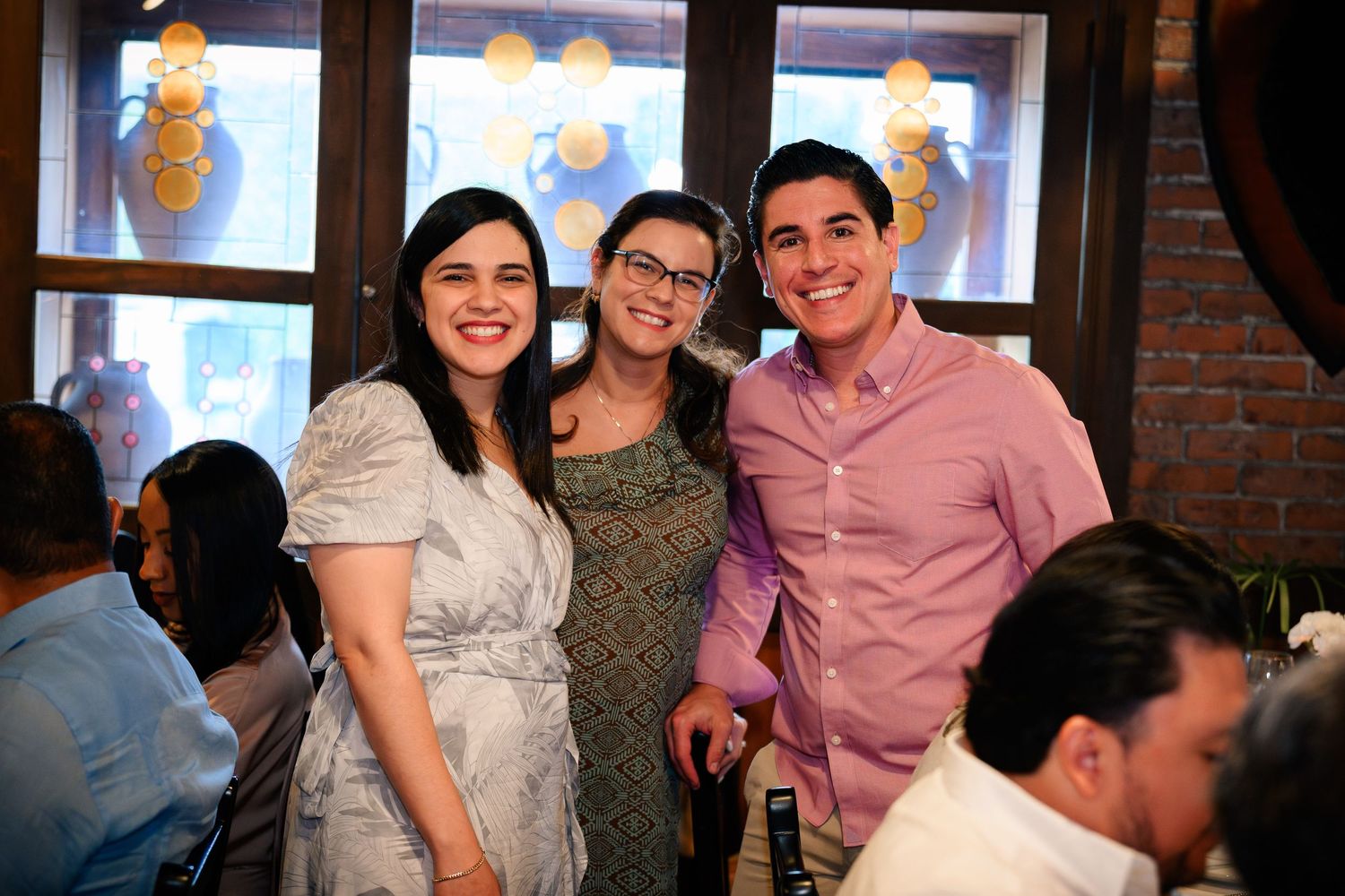 Group of people celebrating at a casual gathering in a restaurant with exposed brick walls and decorative lighting.