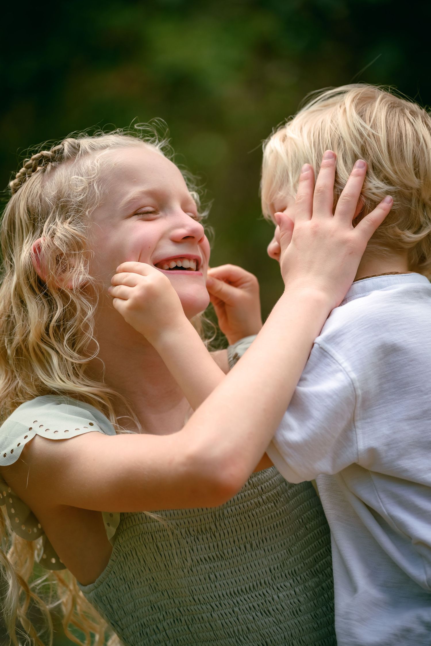 Two young blonde children laughing and playing together outdoors, sharing a joyful moment.