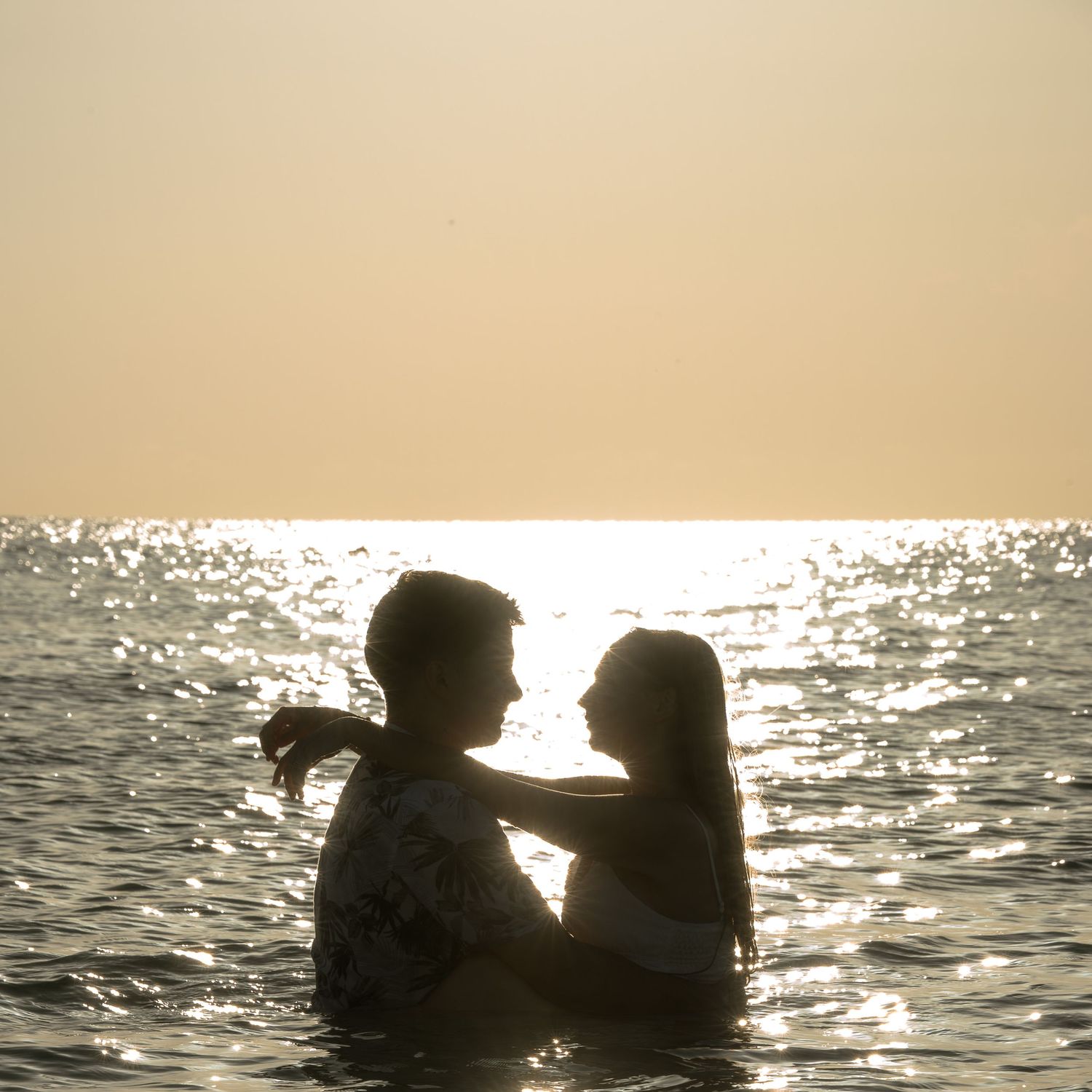 Silhouette of a romantic couple embracing in the ocean at sunset with golden light reflecting on the water.