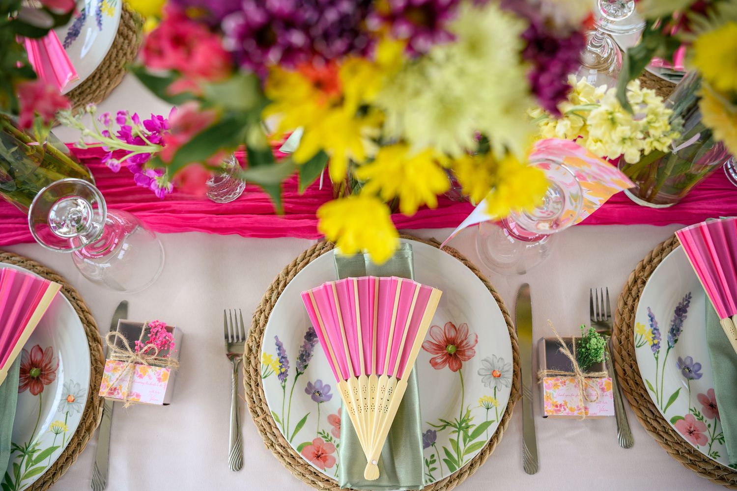 Colorful spring floral table setting with pink napkins, gold-rimmed plates, and vibrant flower arrangements.