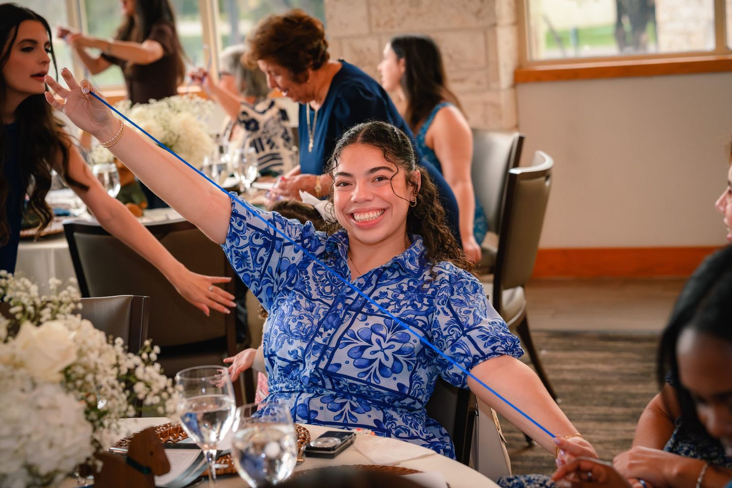 Happy guest in blue floral dress smiling and stretching arms at a baby shower party.